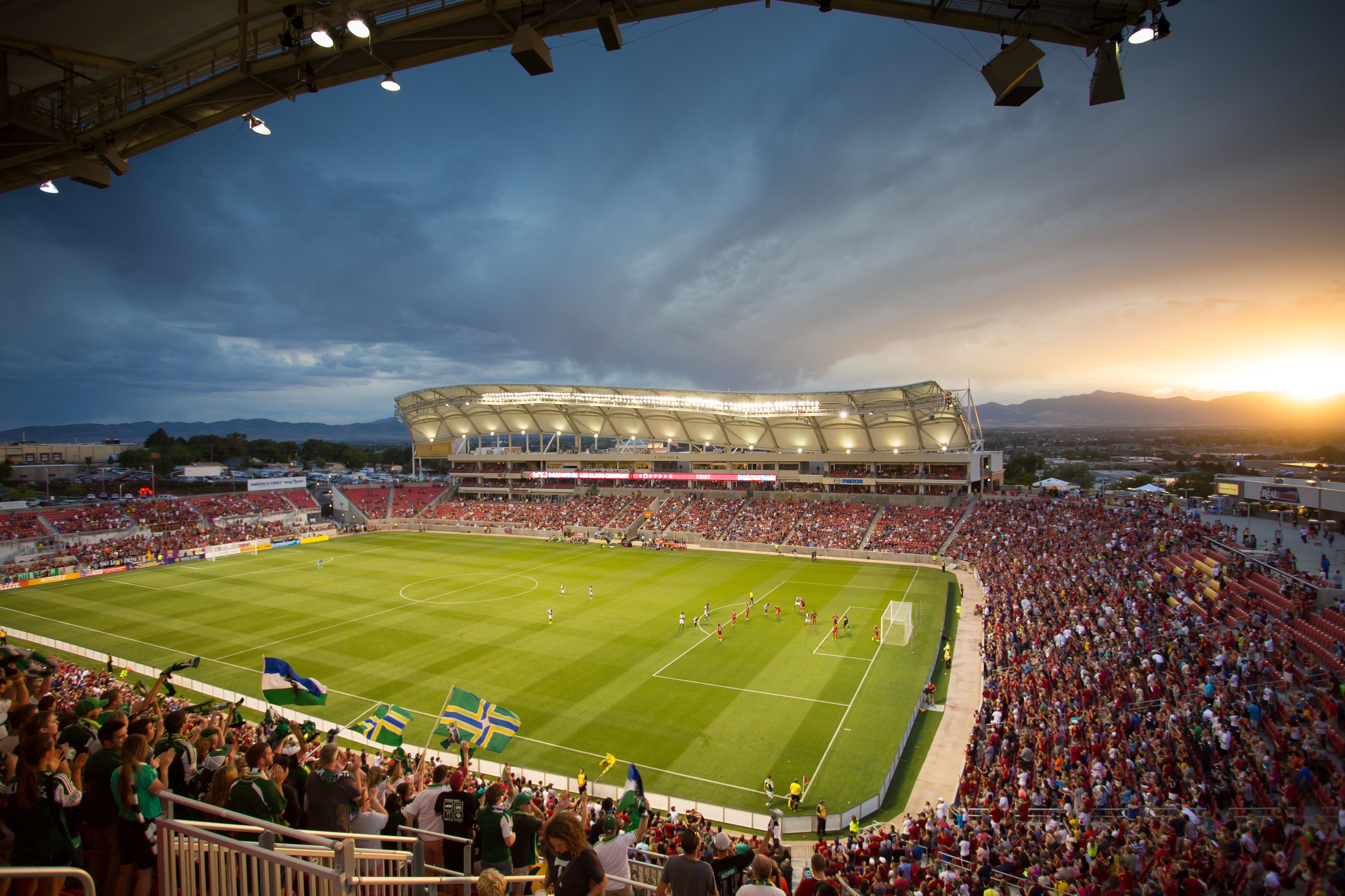 Soccer stadium packed with fans at sunset, mountains visible on the horizon.