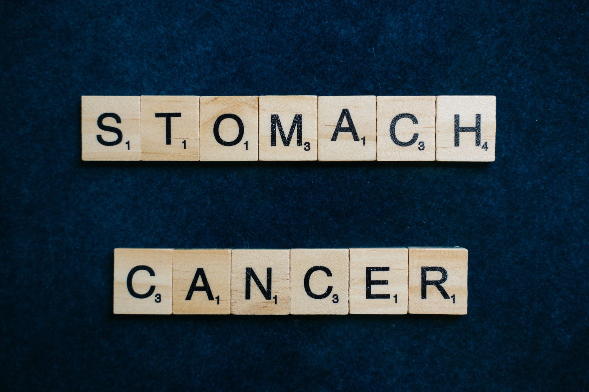 Scrabble tiles spelling 'Stomach Cancer' on a dark blue background, symbolizing awareness.