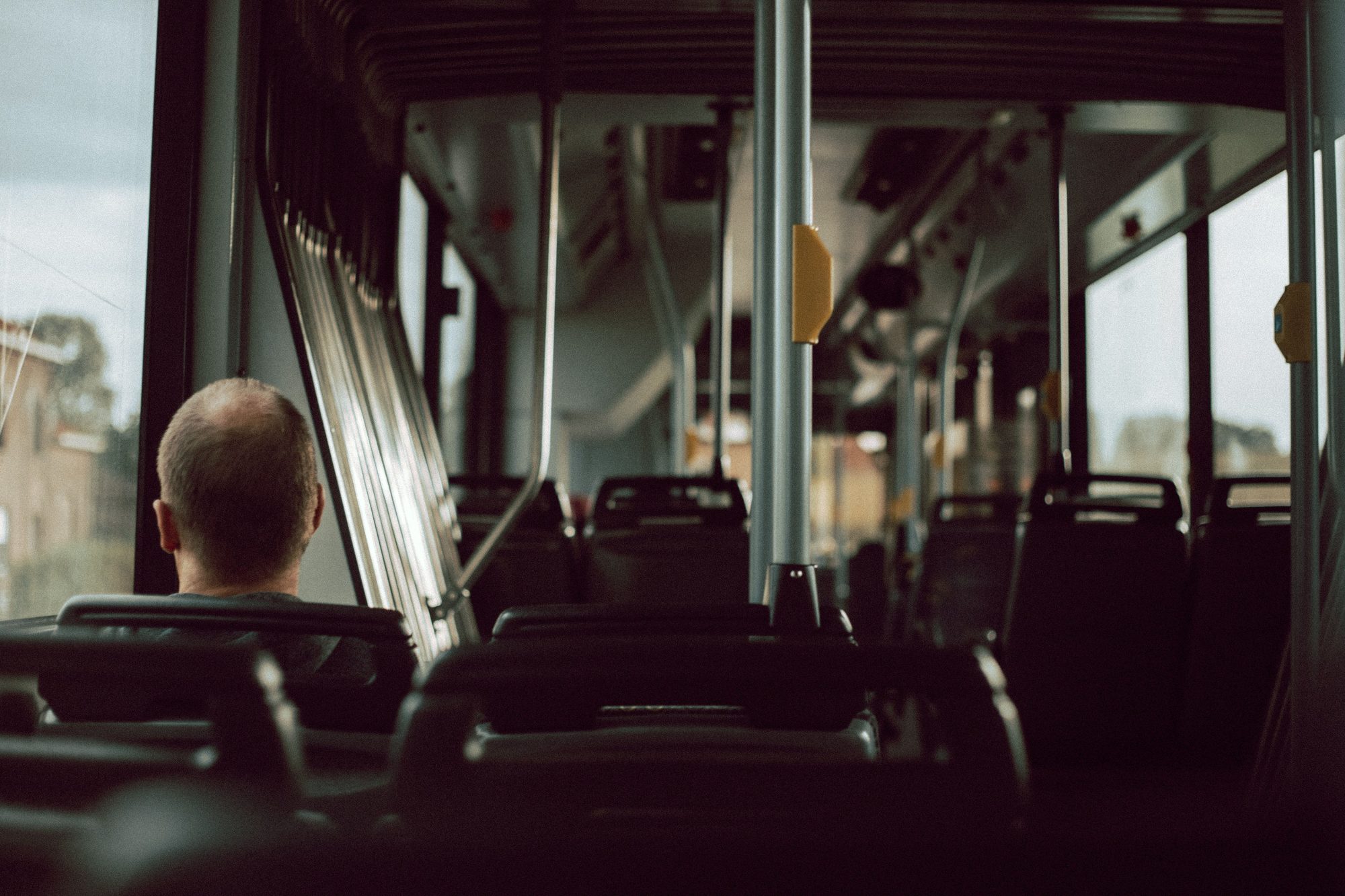 Back view of anonymous male riding on empty bus while sitting on passenger seat near window during trip in city street