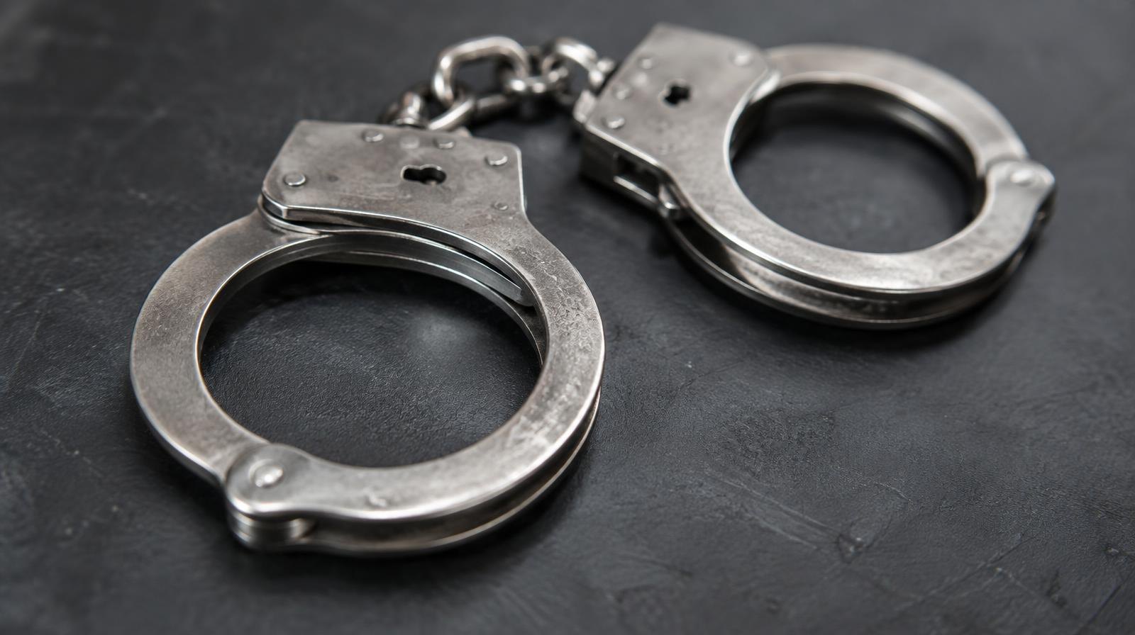 A pair of steel handcuffs resting on a dark surface.