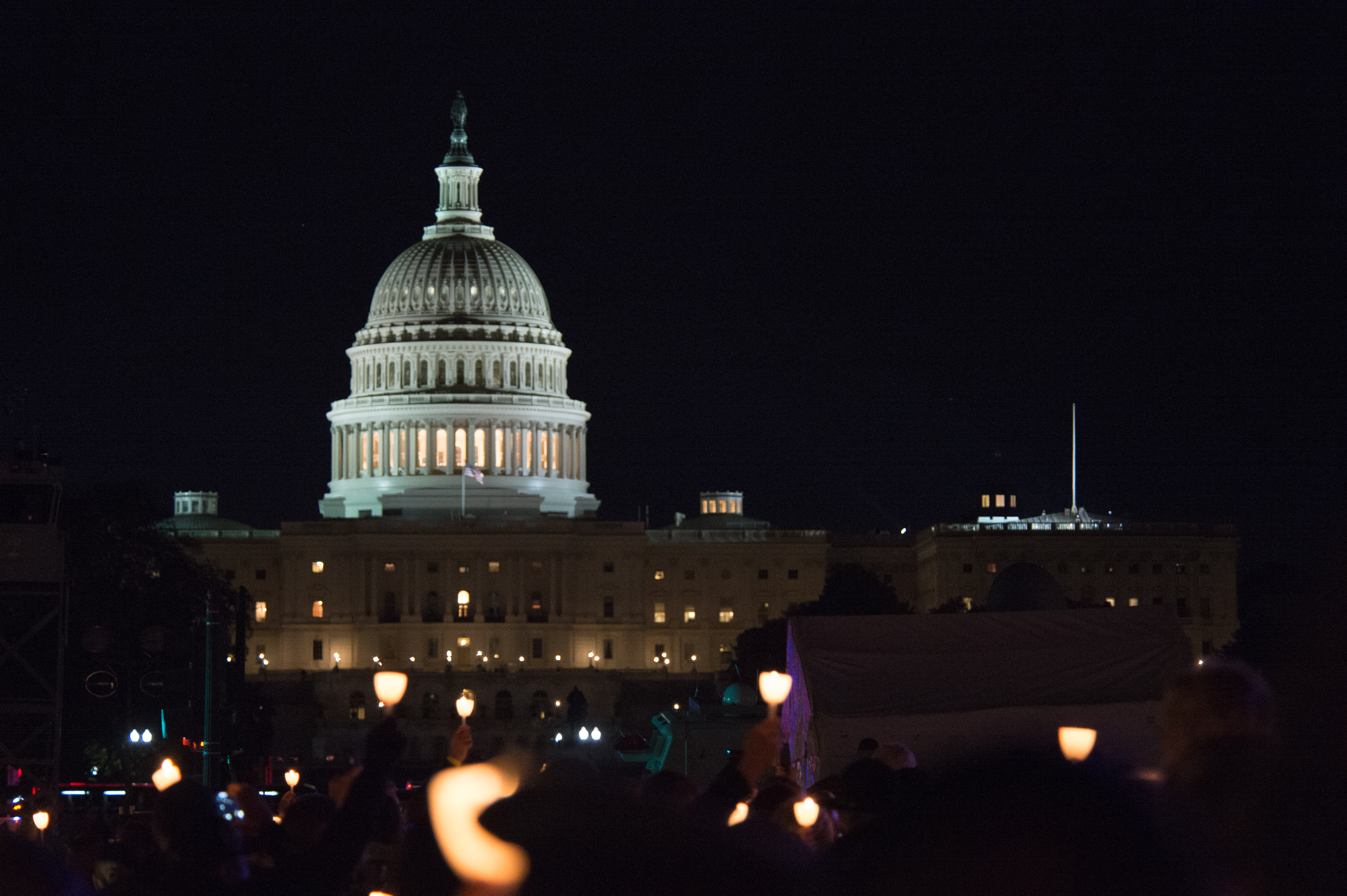 Large crowd holding candles at a nighttime outdoor vigil.