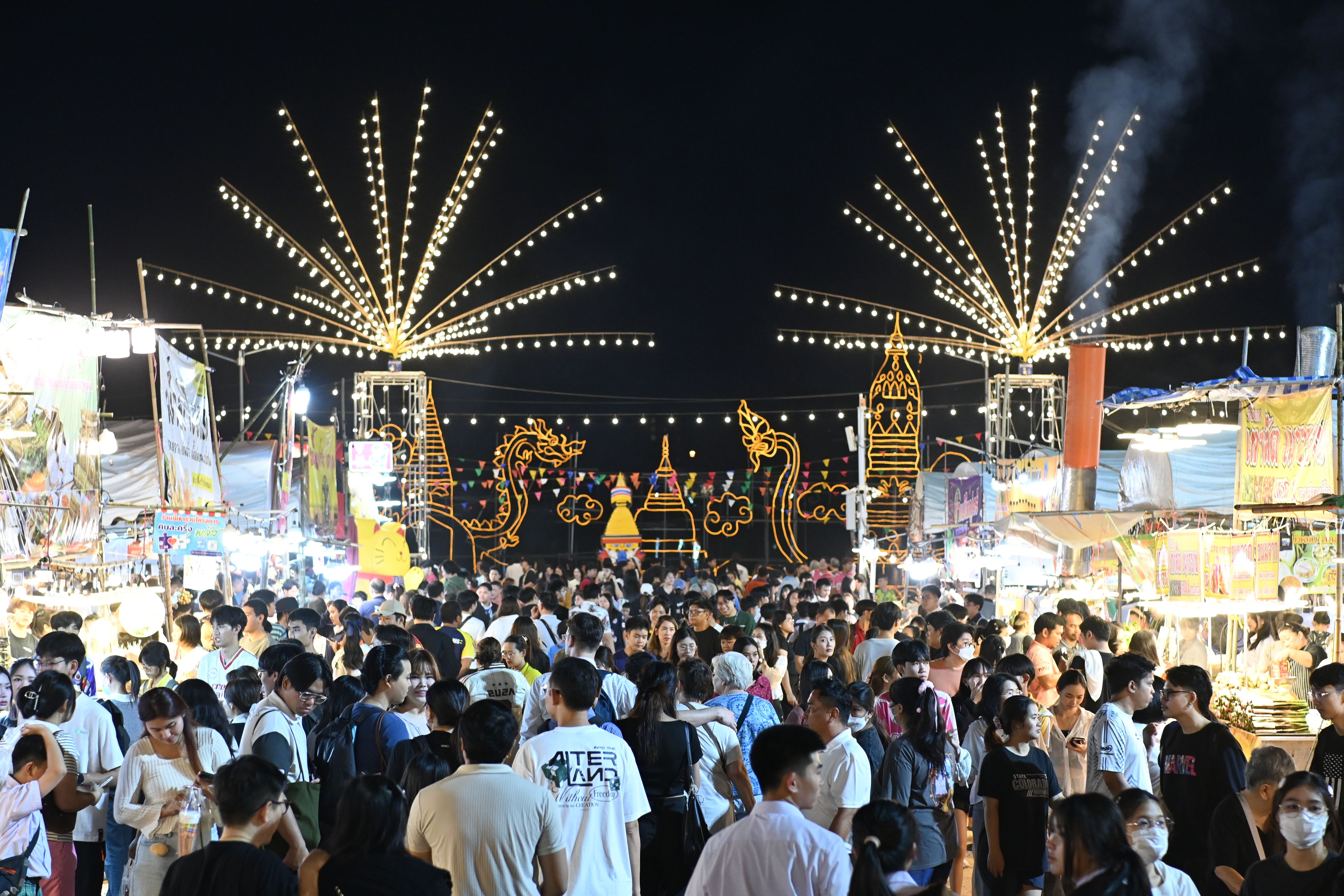 Crowds walk through a brightly lit outdoor night market with starburst string lights overhead.