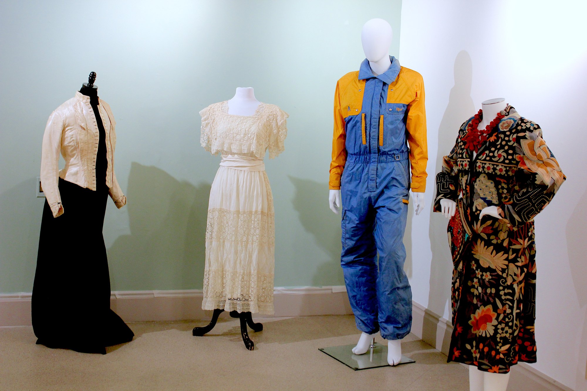 Four mannequins displaying historic women's garments in a museum exhibit space with light green walls.