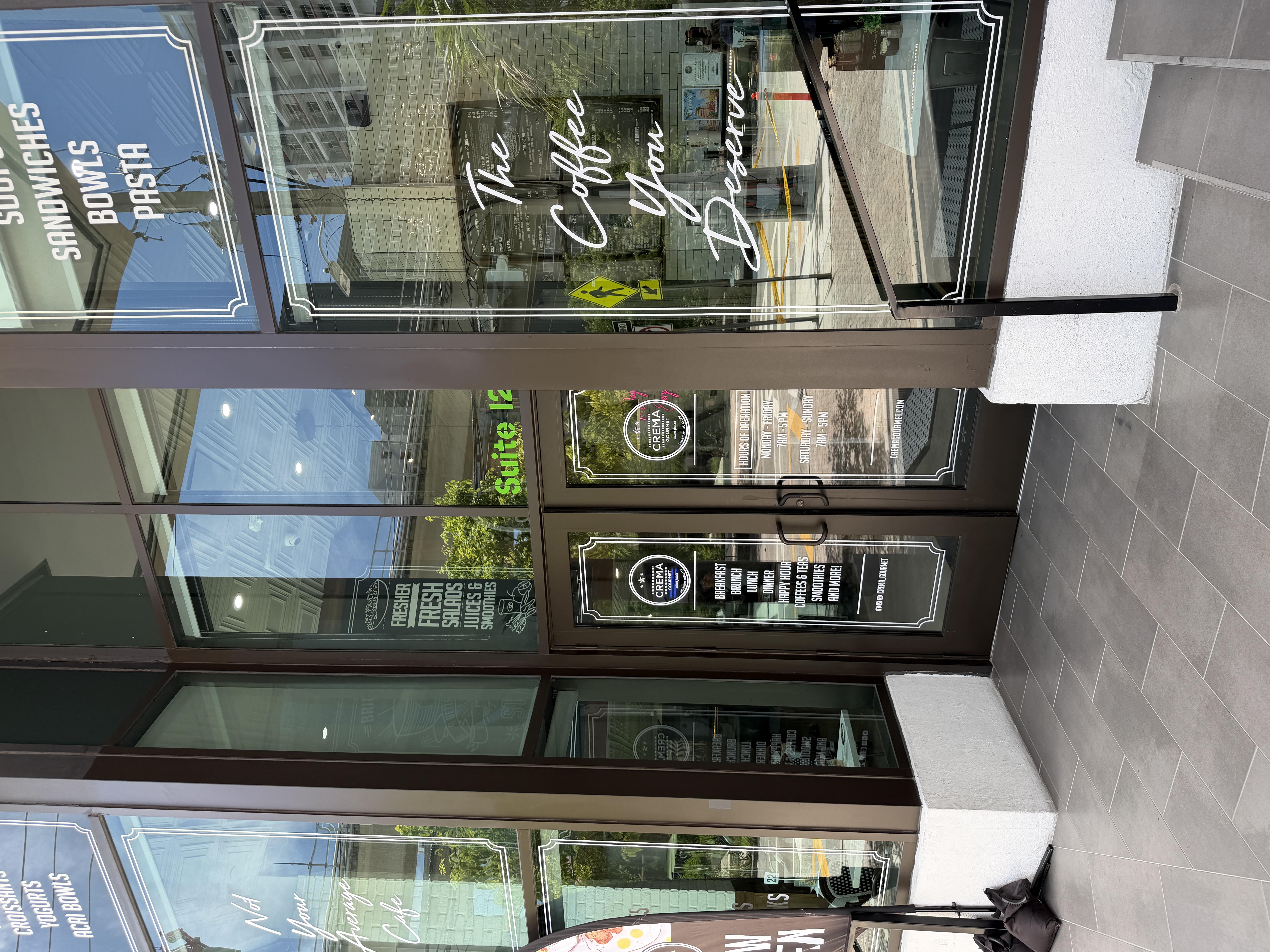 Glass storefront of a Crema Gourmet café with logo and menu items on the windows.