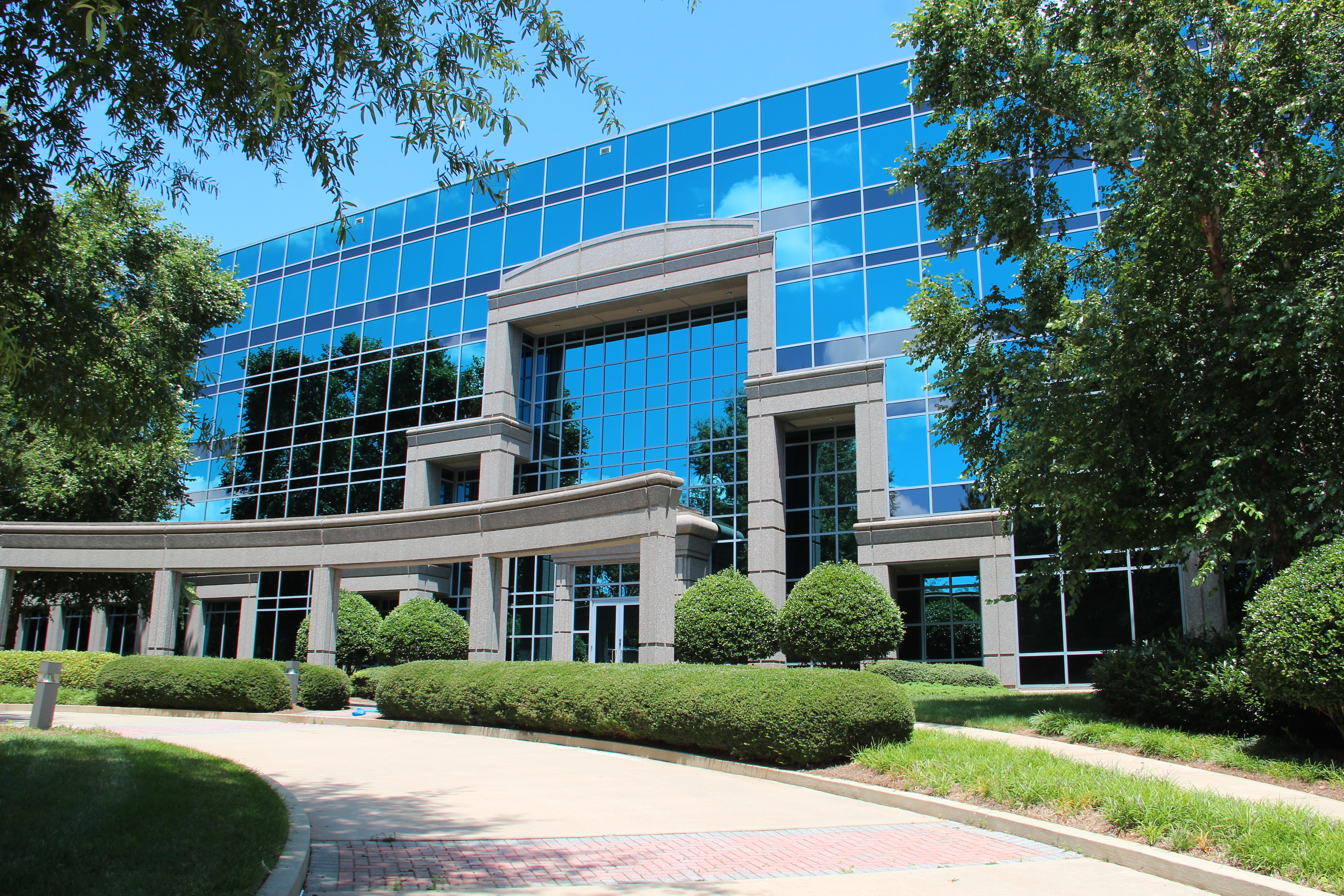 Modern multi-story building with blue glass facade and brick walkway.