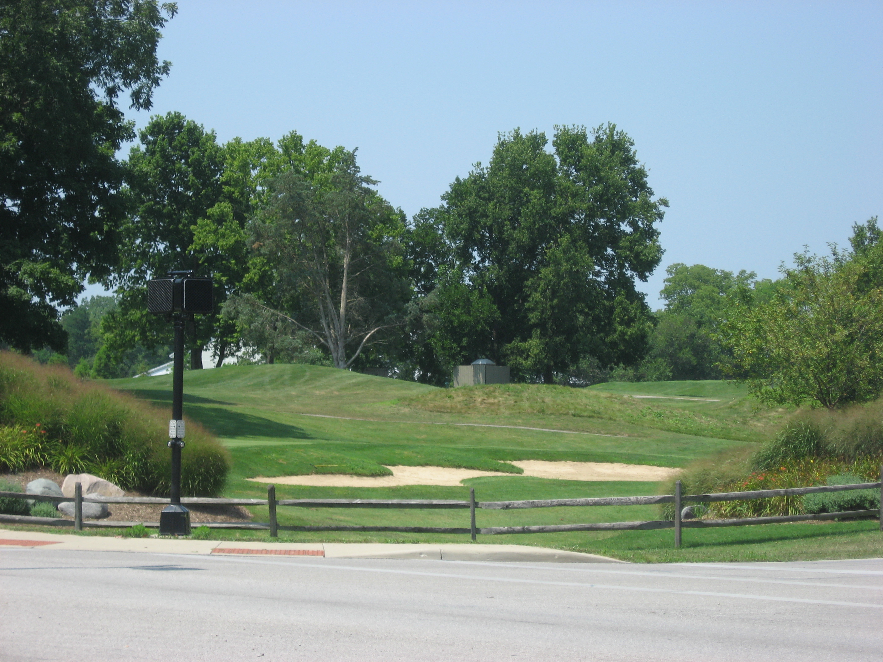 Sunny golf course fairway with sand bunkers and a wooden split-rail fence.