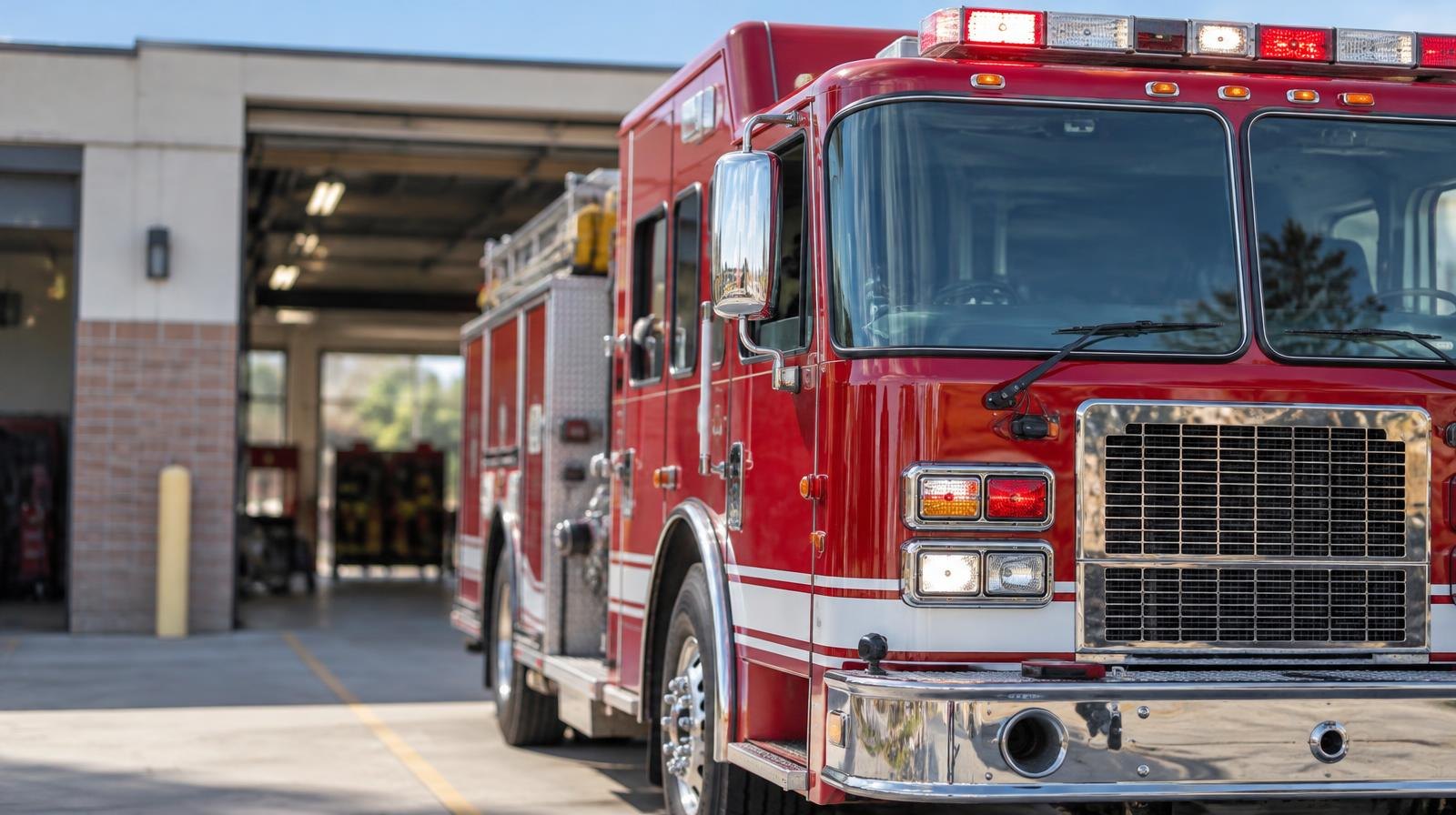 A red fire engine parked in front of an open fire station bay door.