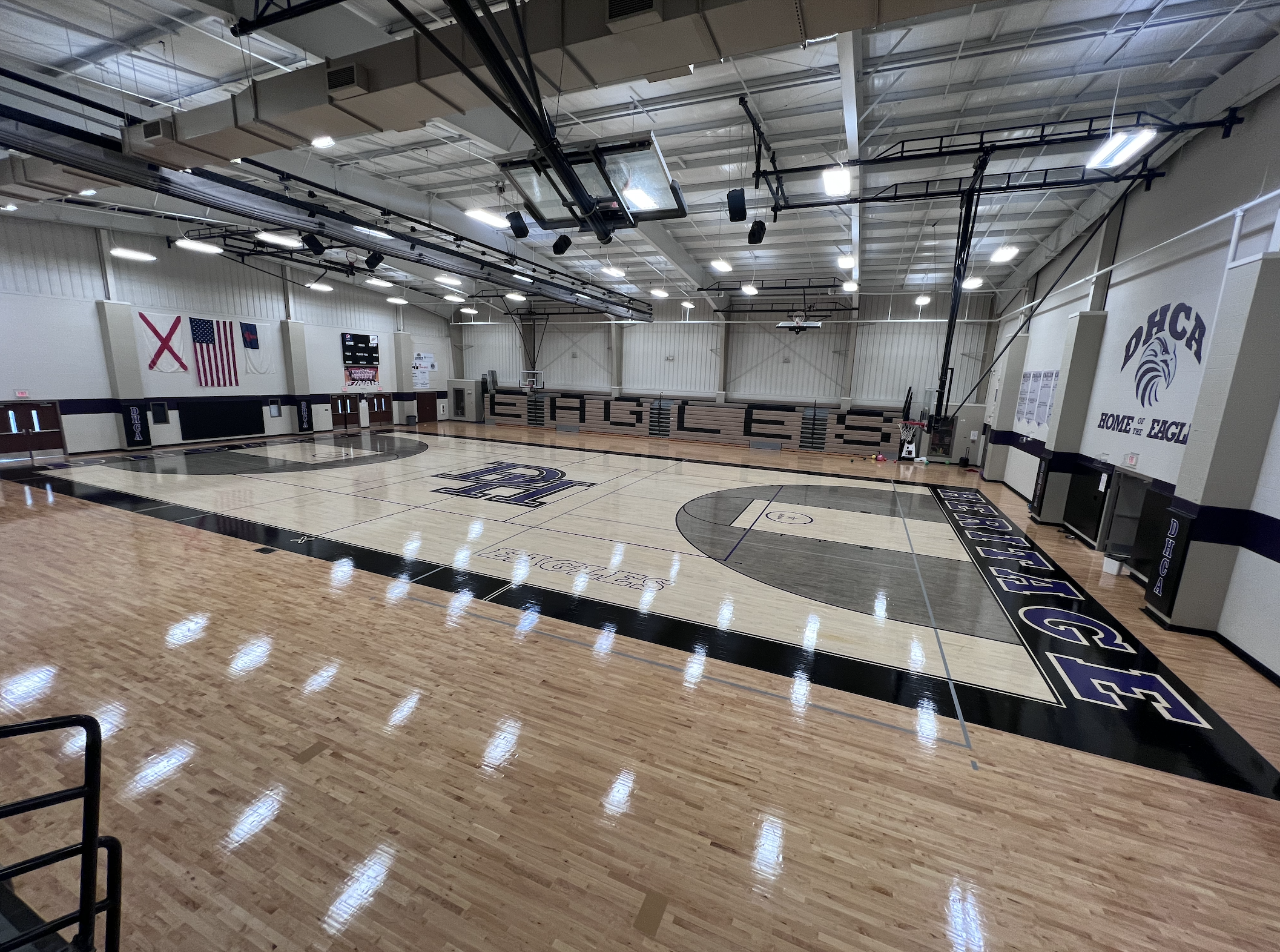 Empty polished hardwood basketball court inside a school gymnasium with bleachers.