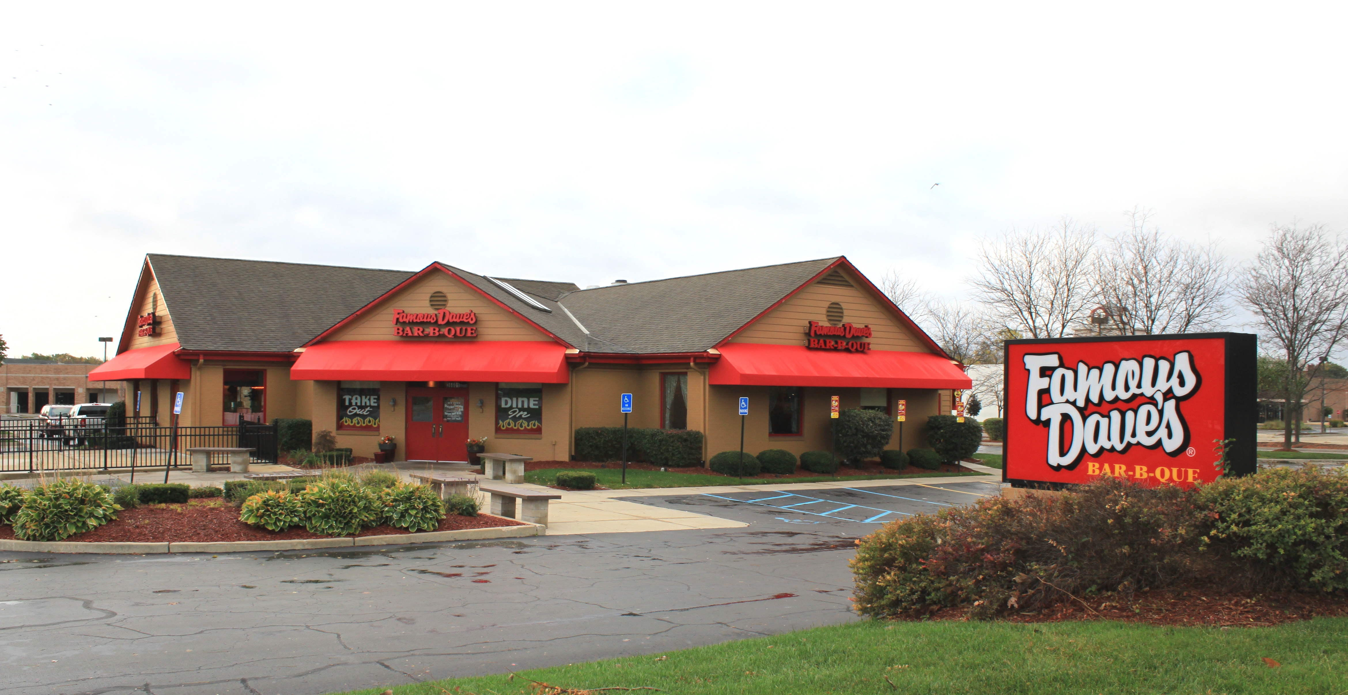Exterior of a Famous Dave's Bar-B-Que restaurant with red awnings and a roadside sign.