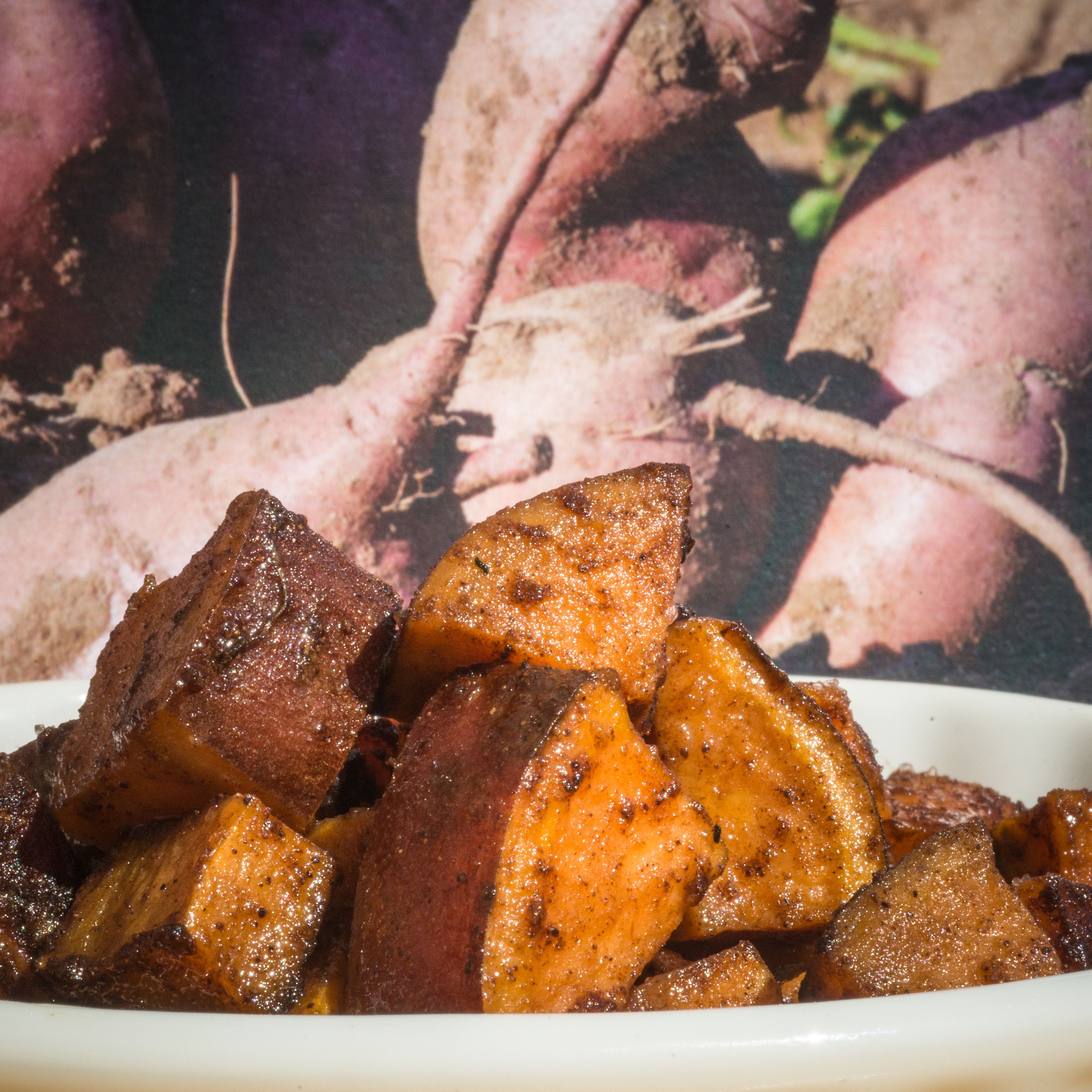 A white bowl filled with roasted, caramelized sweet potato cubes on a wooden surface.
