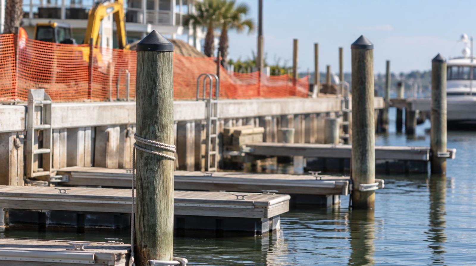 Marina dock with wooden pilings and floating piers next to a fenced seawall.