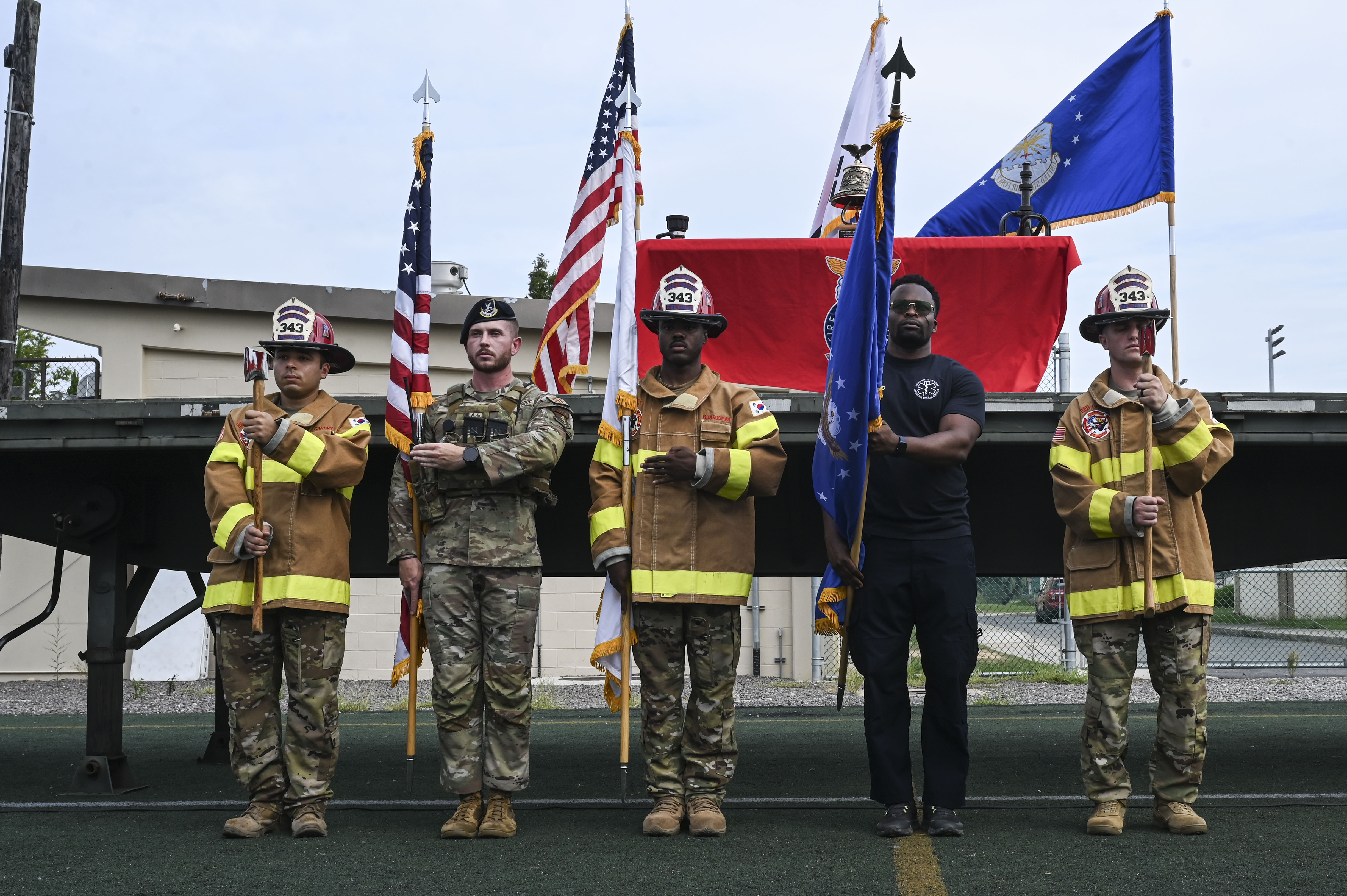 Military and firefighter honor guard holding flags at an outdoor 9/11 ceremony.