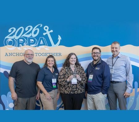 Group of five adults posing in front of a blue conference backdrop, one holding a small award plaque.