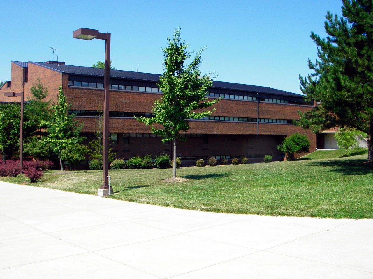 Multi-story red brick school building with green lawn and trees under a clear blue sky.