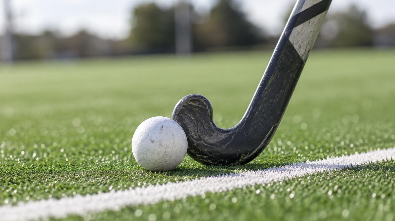 A field hockey stick and ball resting on green artificial turf beside a white line.