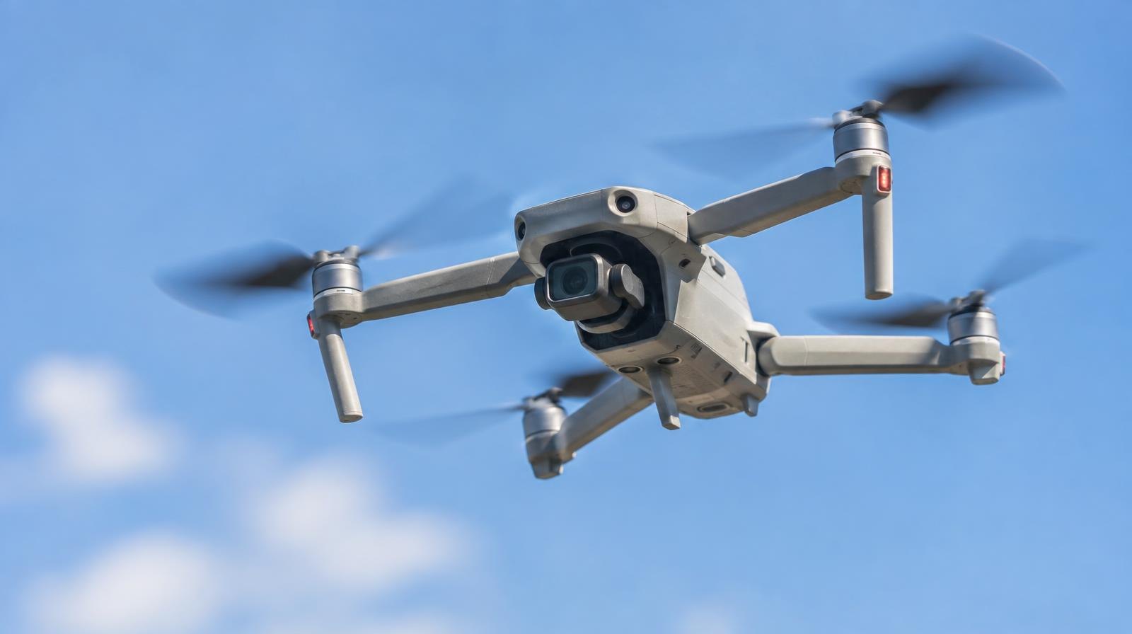 A quadcopter drone hovering against a clear blue sky.