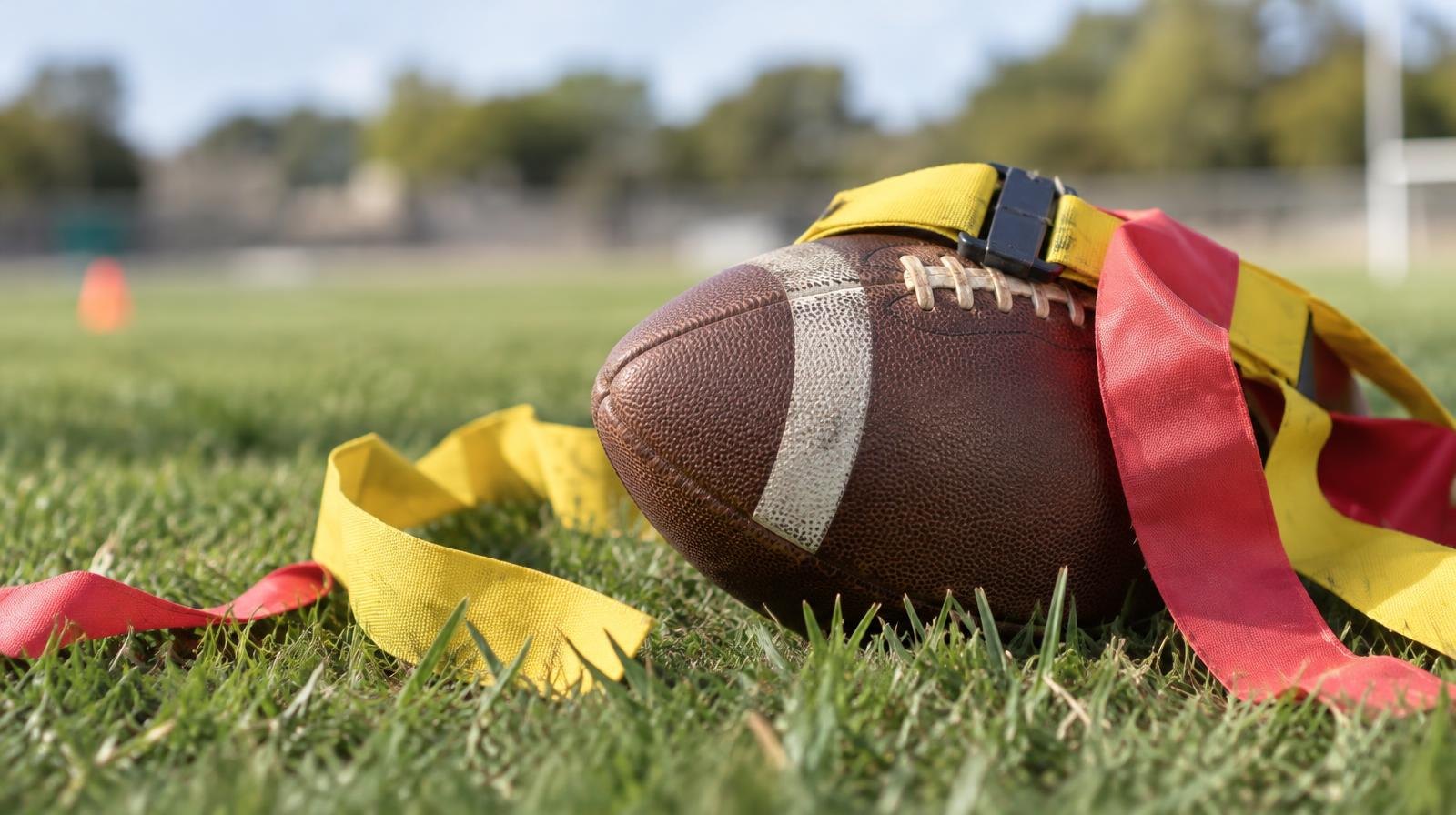A football with colorful flag football belts and flags resting on green grass.