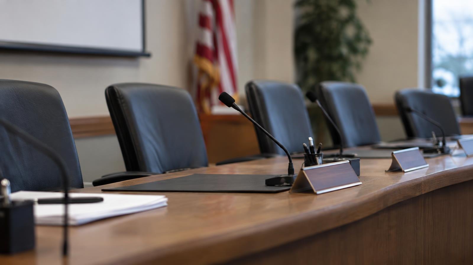 Empty conference table with chairs, name placards, and a microphone in a meeting room.