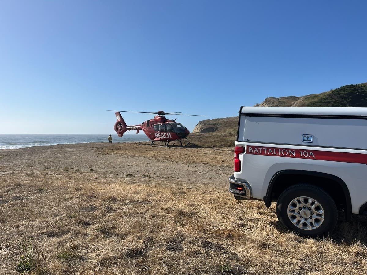 A red REACH helicopter landed on a coastal bluff next to a white fire department pickup truck.