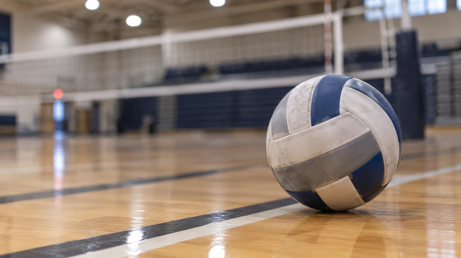 A volleyball resting on a hardwood gym floor near the net.