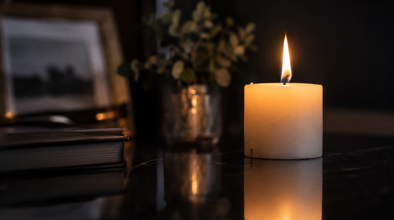 A single white candle burning with its flame reflected on a polished surface.