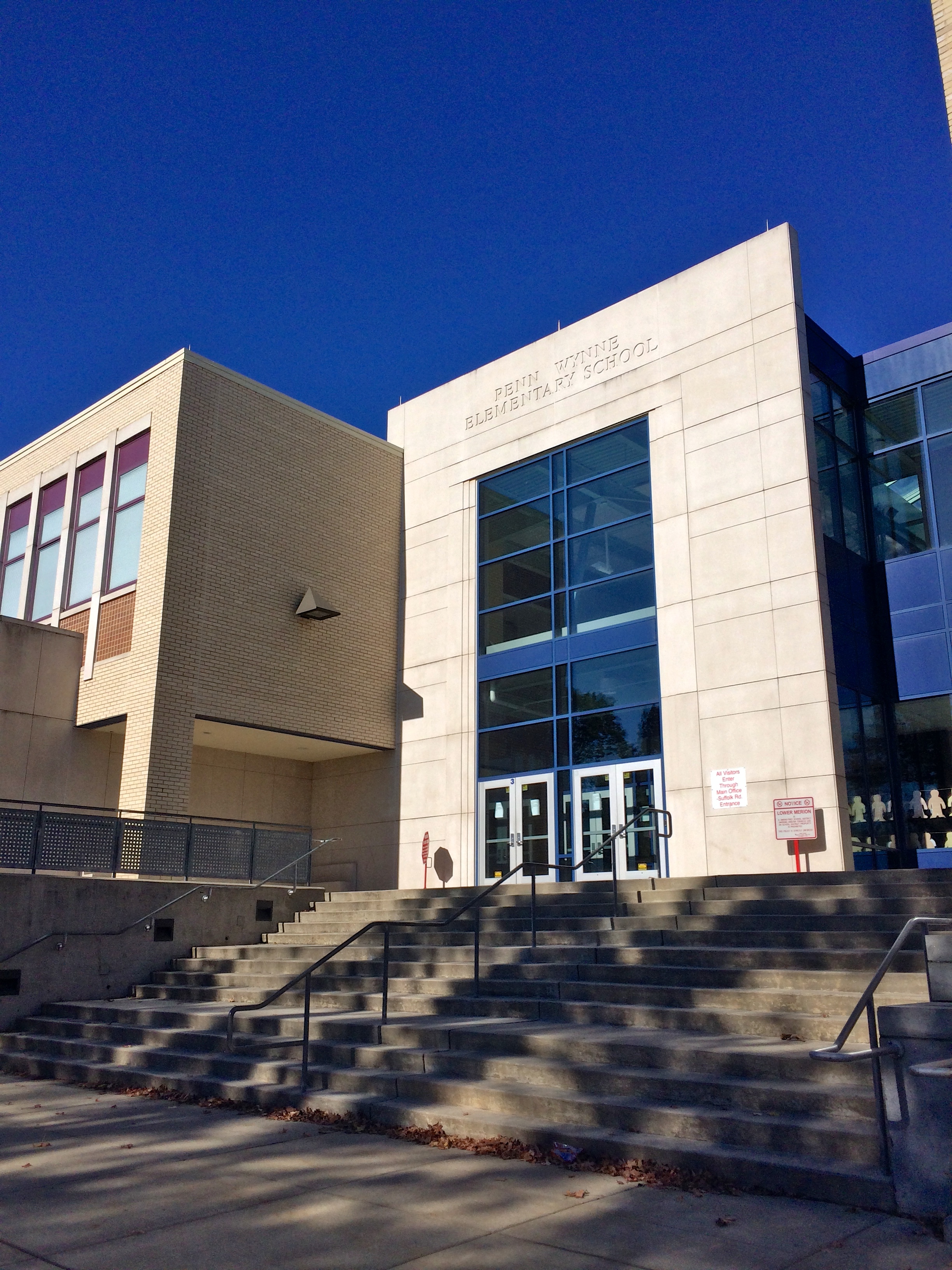 Exterior entrance of a modern brick and glass elementary school building under a clear blue sky.
