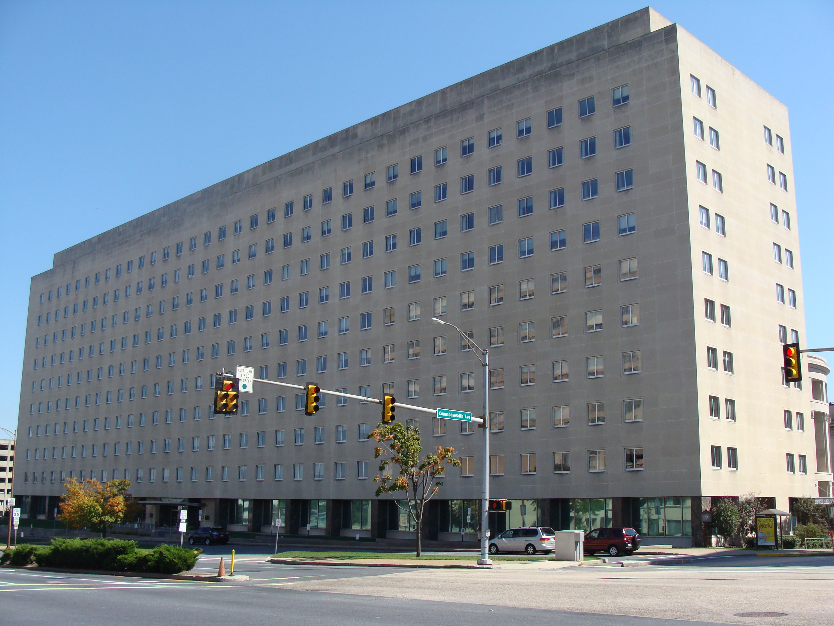 Tall beige government office building at a Harrisburg street corner under blue sky.