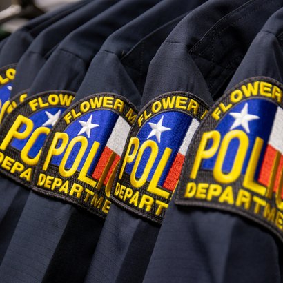 Row of navy blue police uniform shirts with embroidered department patches on hangers.