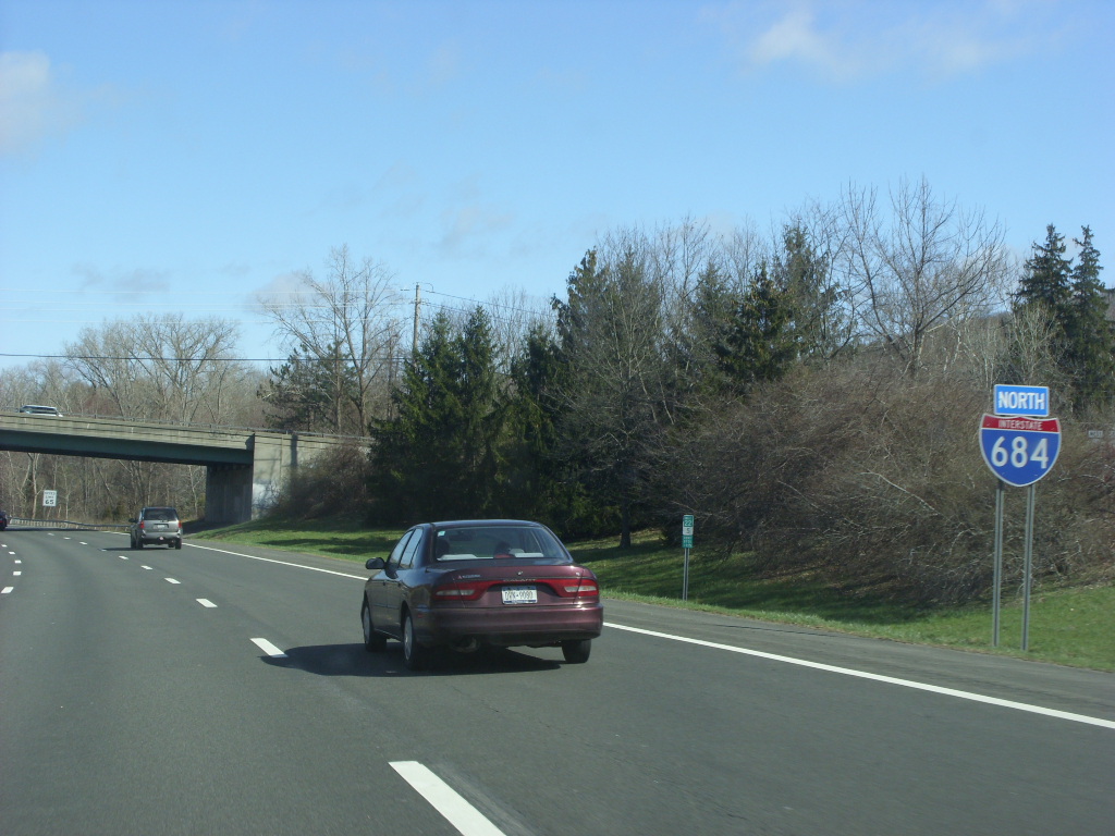 A car traveling northbound on a multi-lane highway with a blue interstate sign on the right.