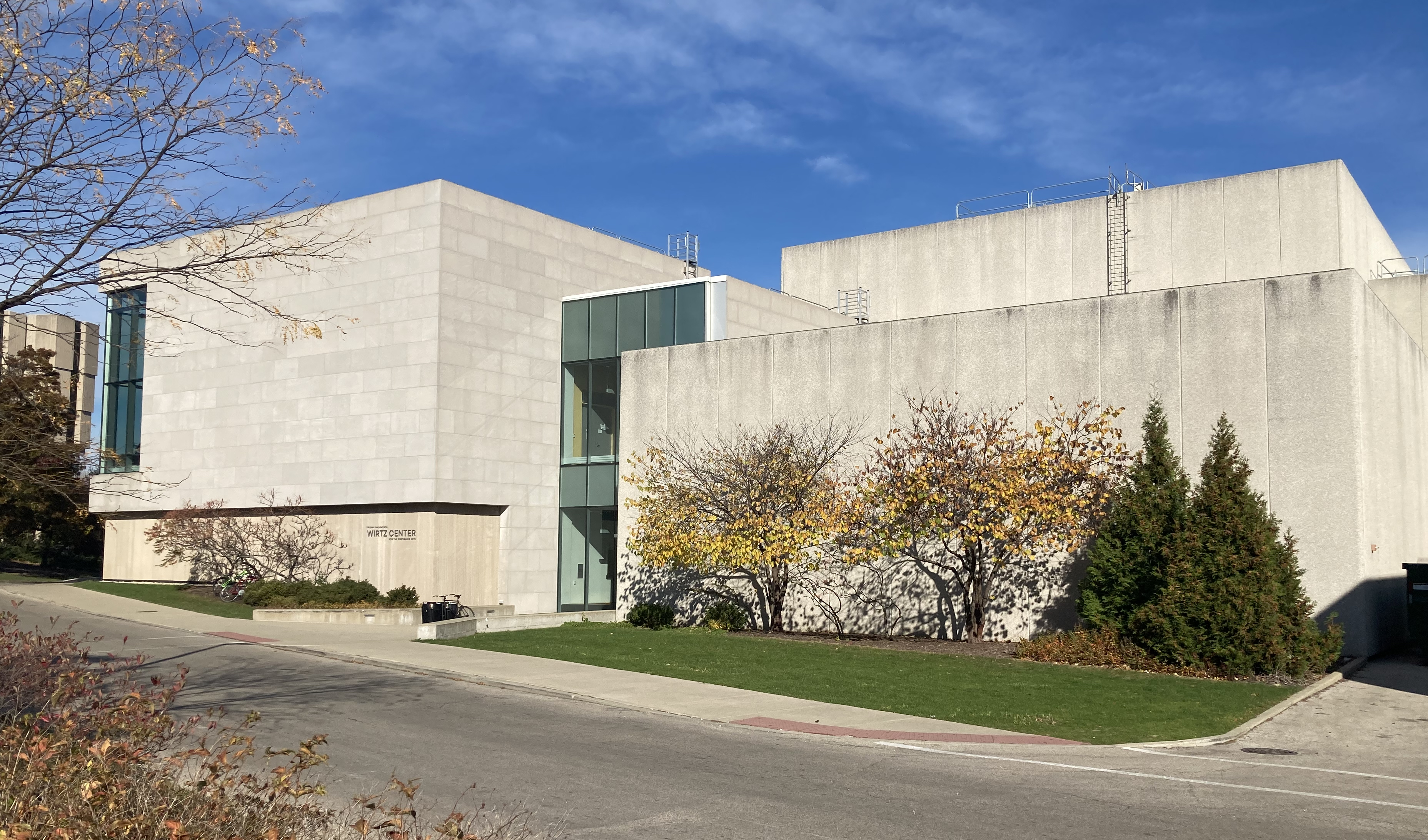 Modernist concrete performing arts building with glass entryway and autumn trees.