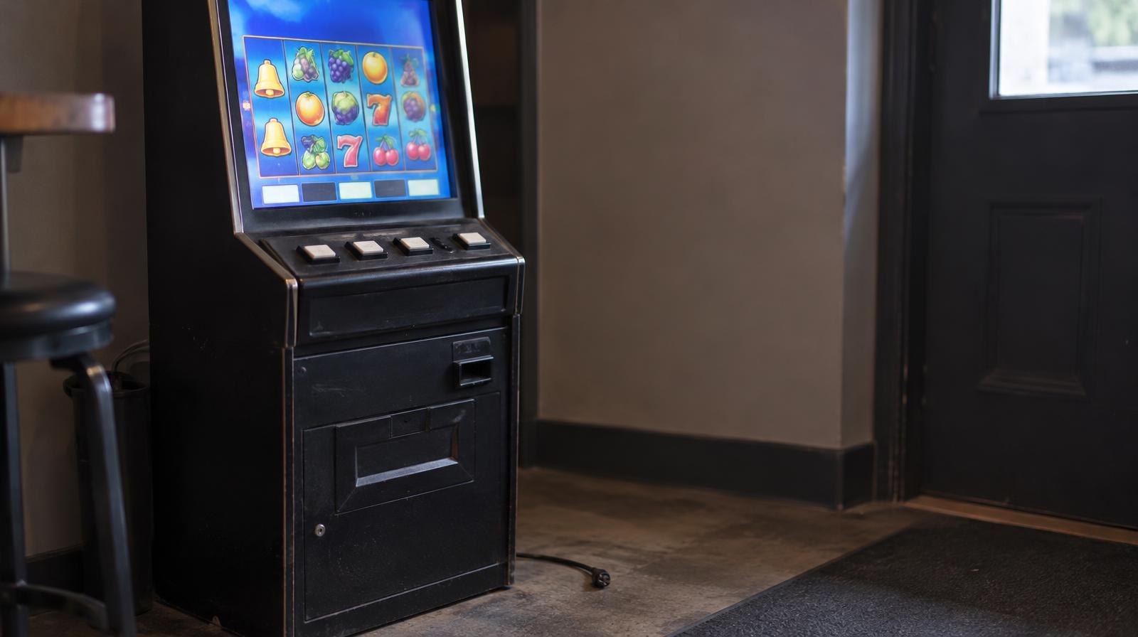 A standalone electronic gaming terminal with a glowing screen near a door.