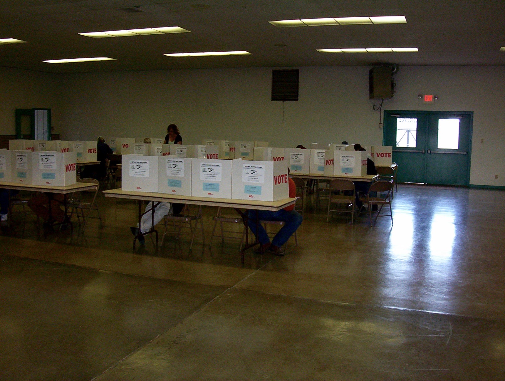 Rows of white voting booths labeled VOTE on tables in a mostly empty hall.
