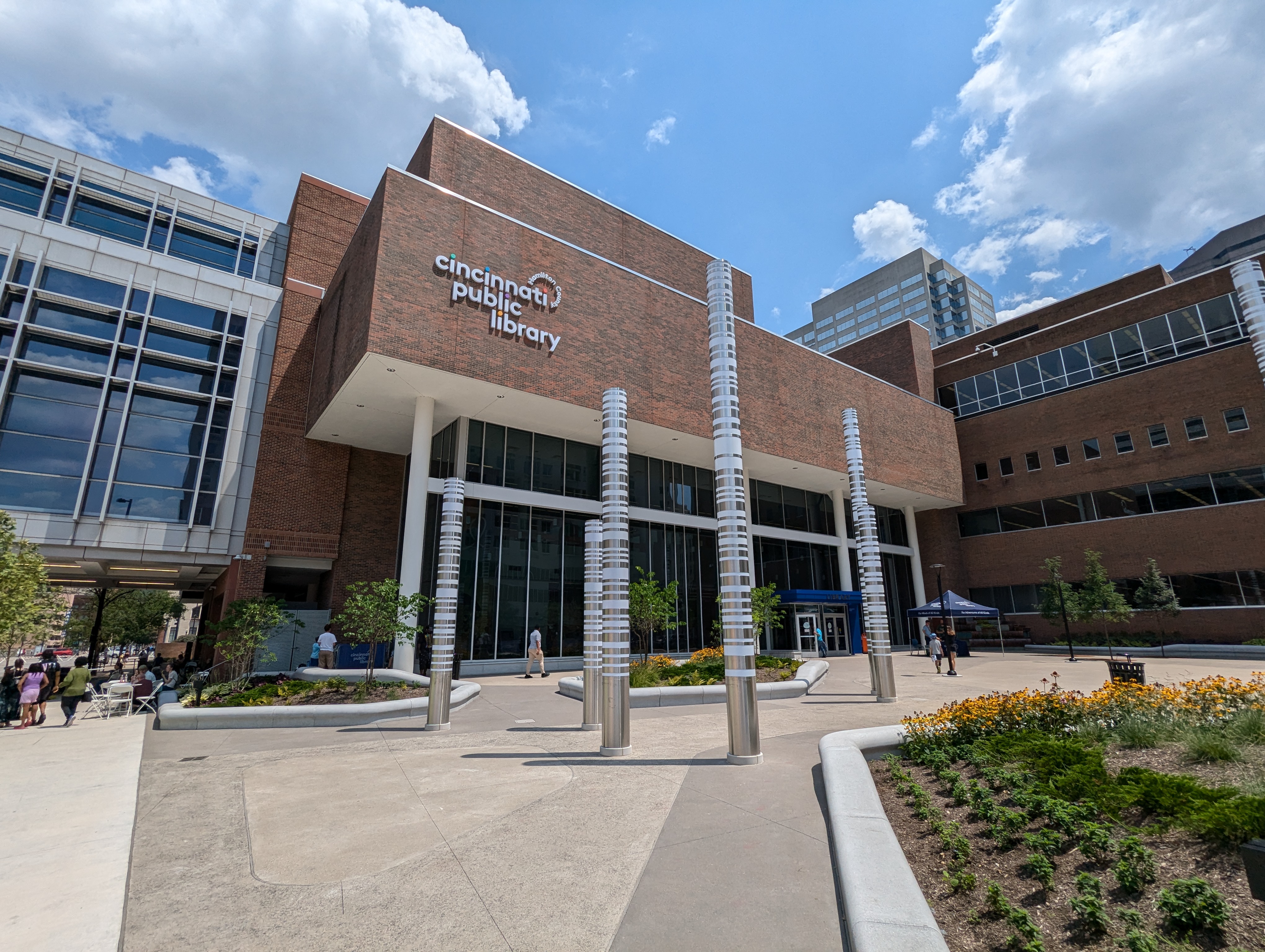 Exterior of a modern brick library building with large glass windows and decorative metal plaza columns.