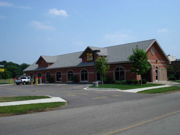 Exterior of a brick automatic tunnel car wash building with drive lanes and parking lot.
