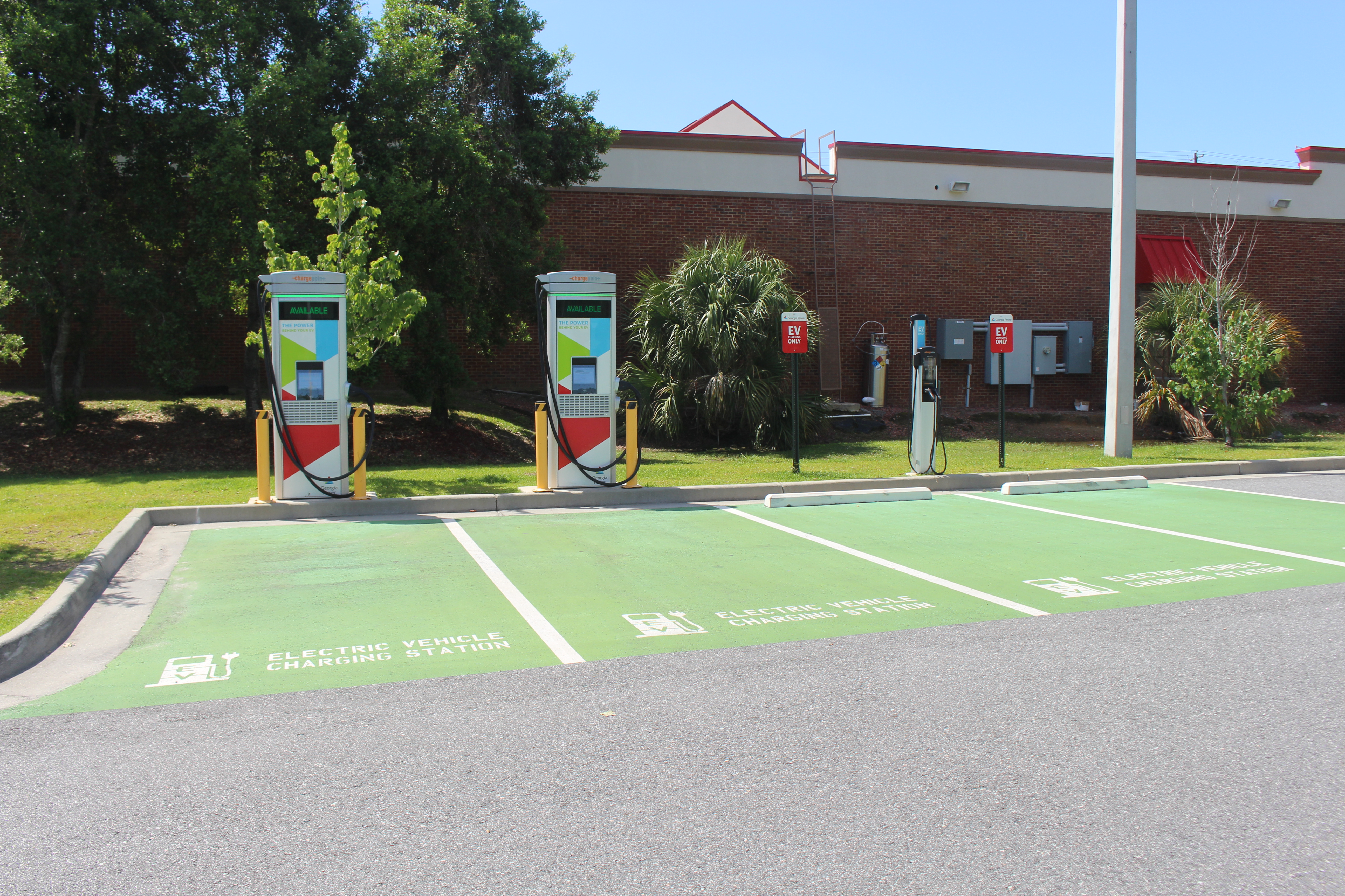 EV charging station pedestals in green-marked parking spaces outside a brick building.