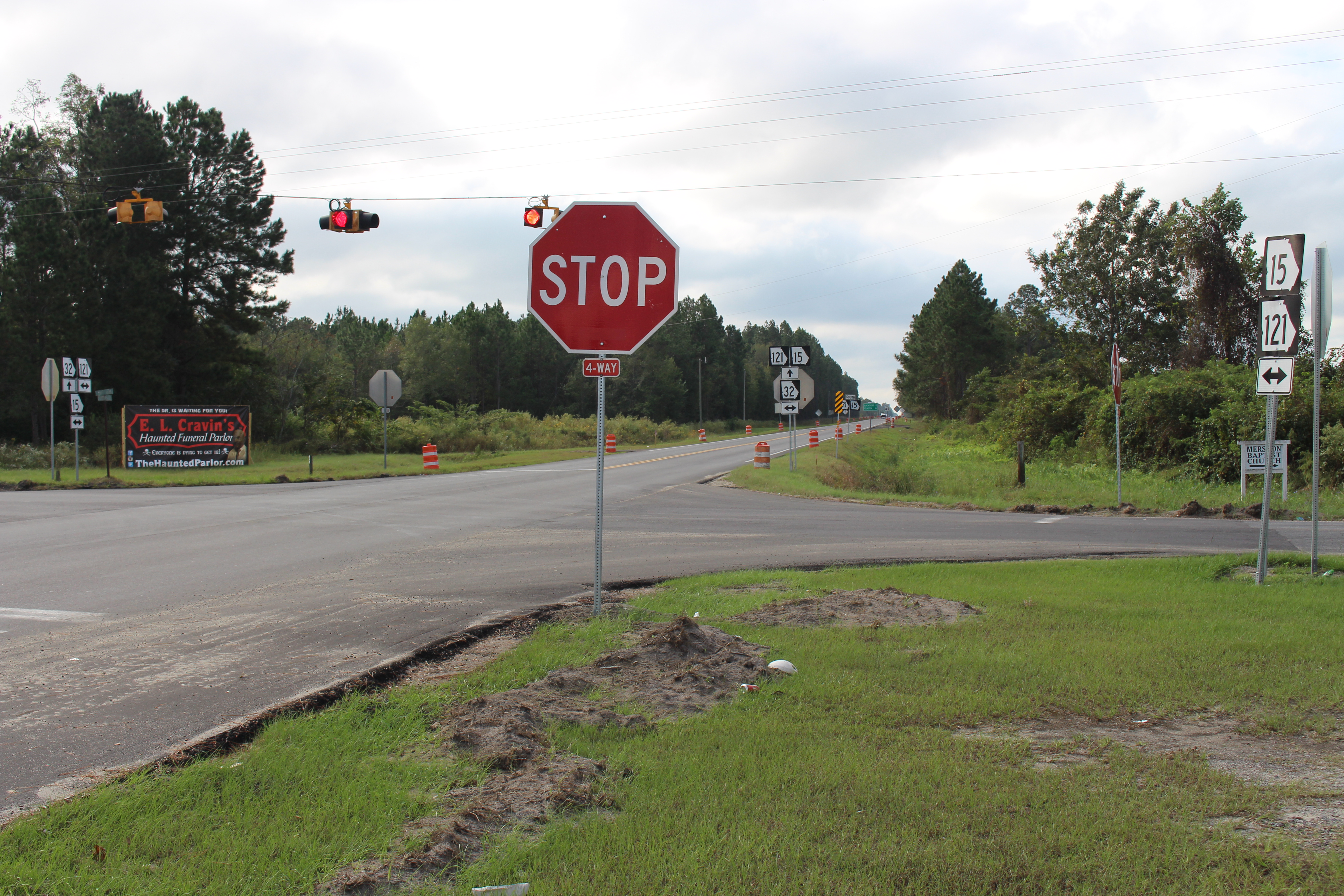 Red stop sign on a metal post at a rural road intersection with a flashing signal behind it.