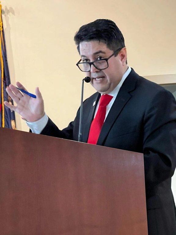 Man in suit and red tie speaking at podium.