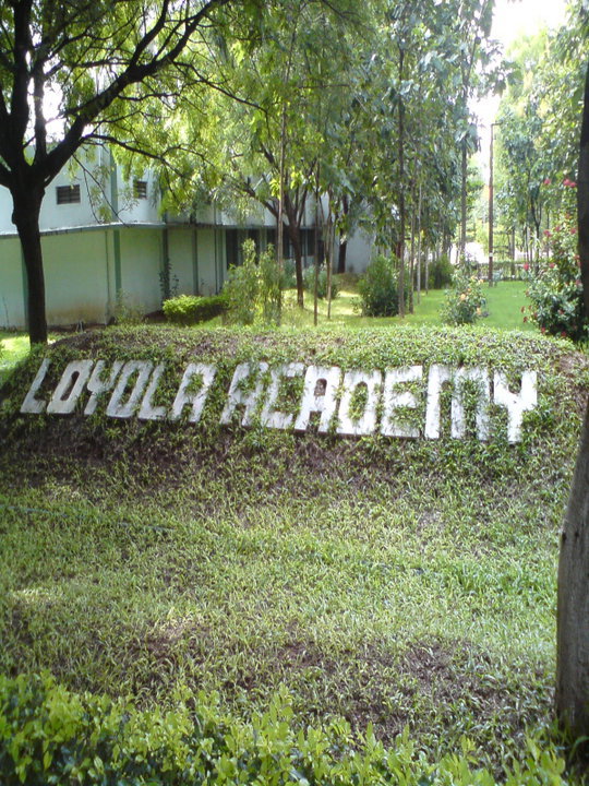 Large white letters spelling Loyola Academy on a grassy hillside with trees behind.