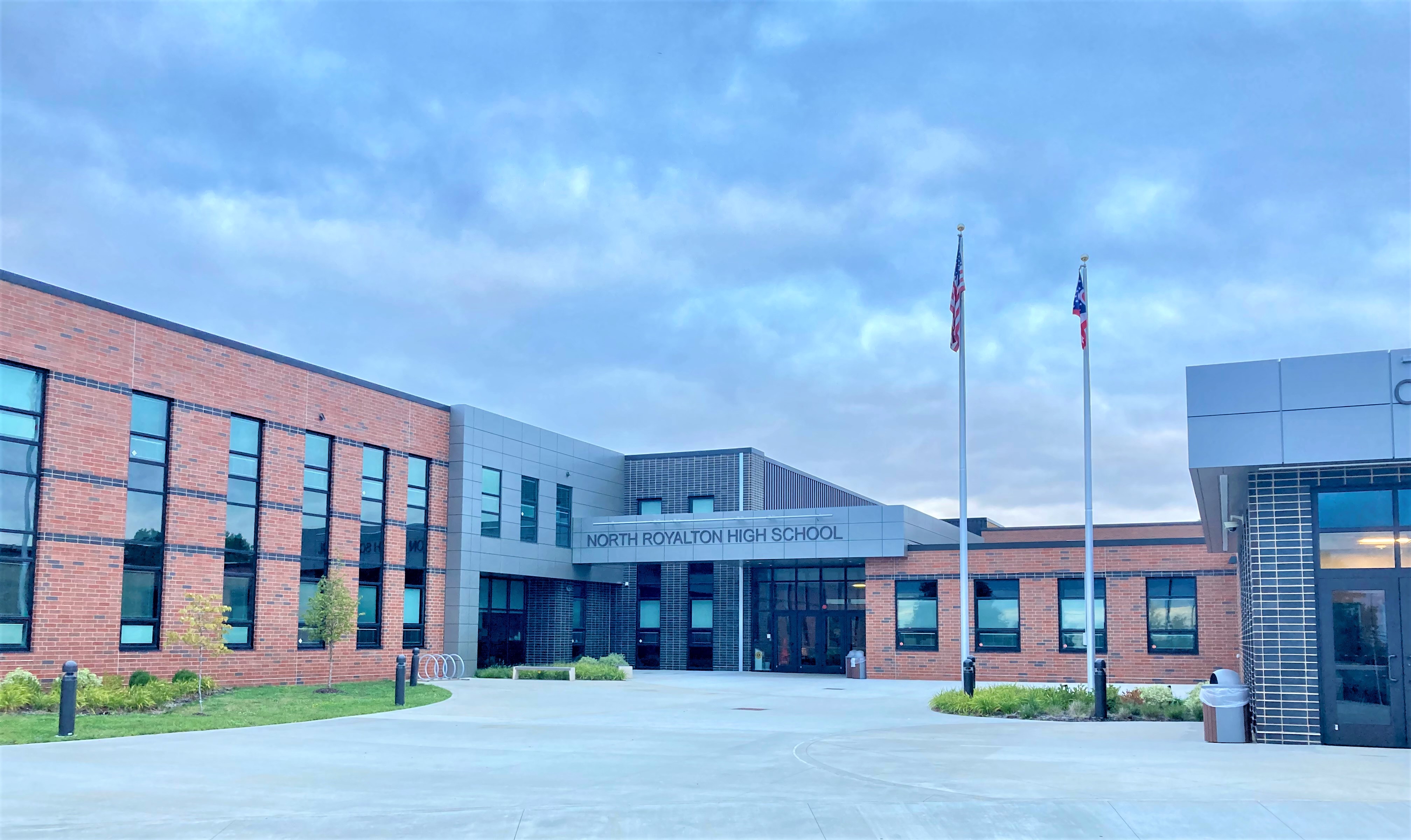 Exterior front entrance of a red brick high school with two flagpoles.