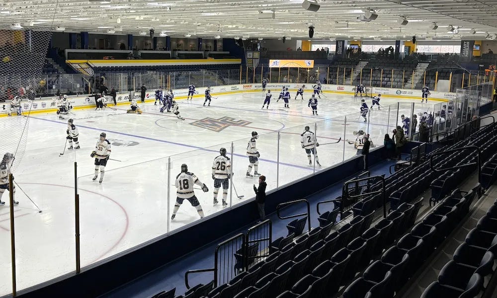 Hockey players in dark and light uniforms warming up on an indoor rink before a game.