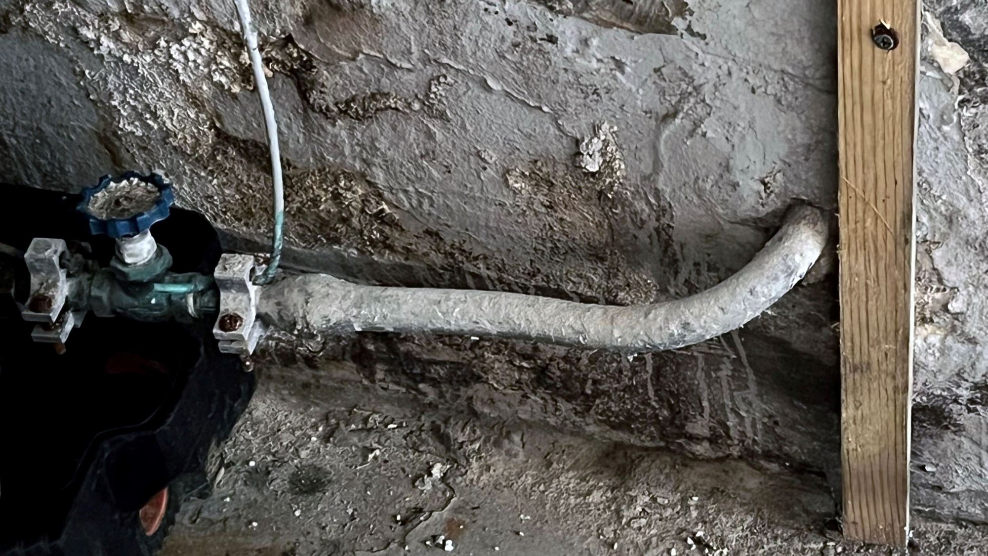 Heavily corroded metal pipe connected to a shutoff valve on a concrete basement wall.
