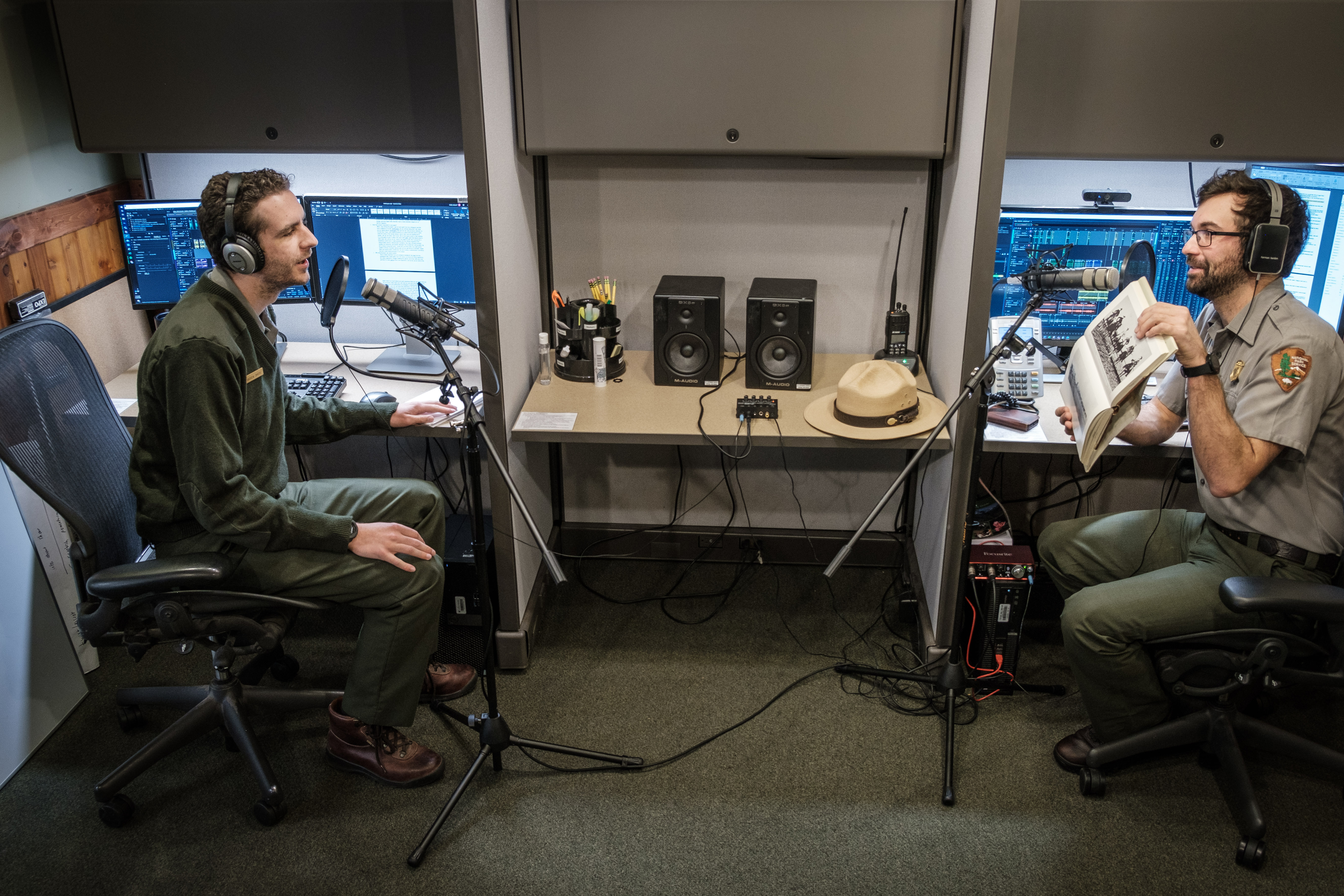 Two people wearing headphones speak into microphones in a podcast recording studio.