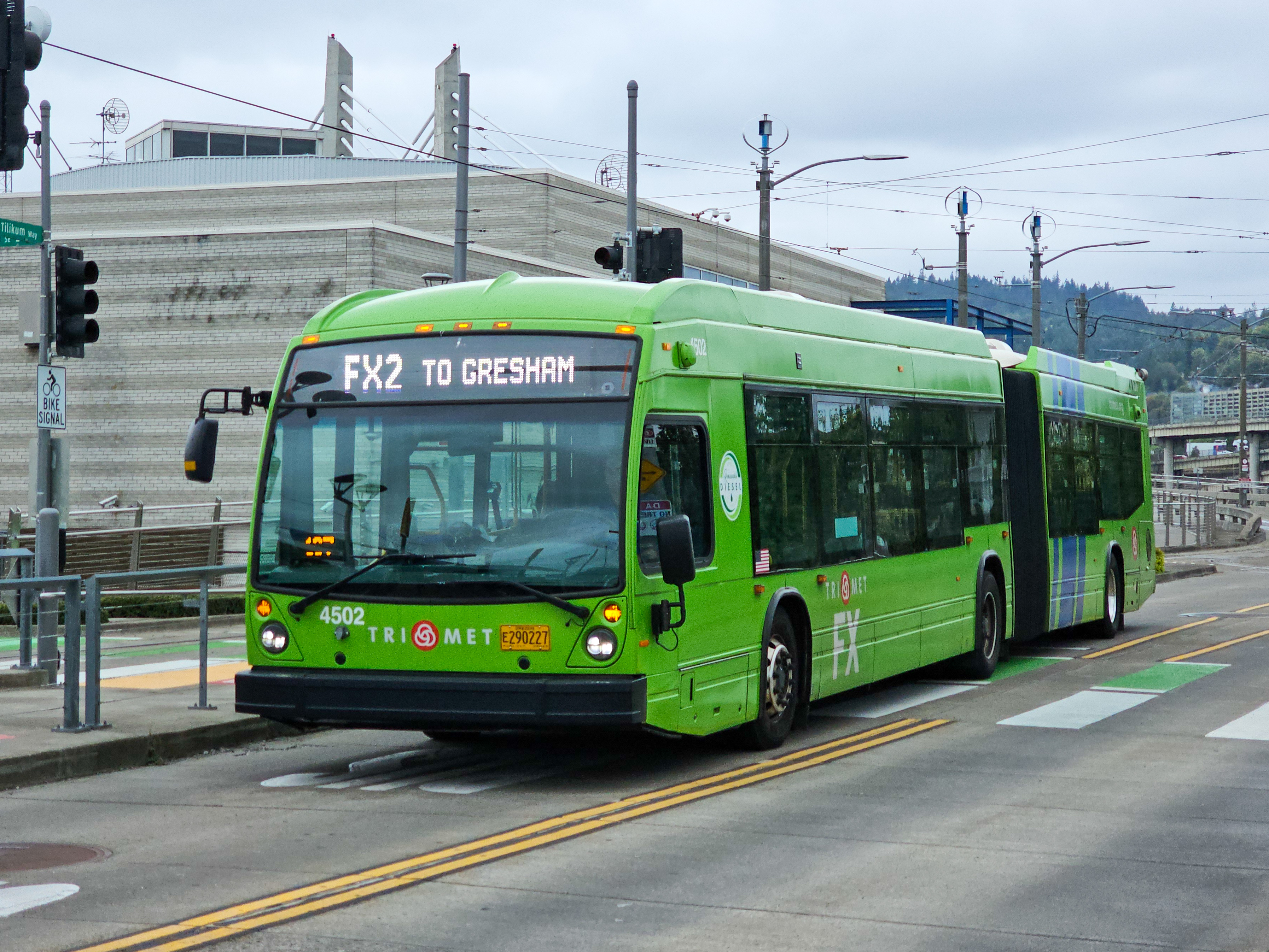 A green TriMet articulated bus at a transit station with overhead wires visible.