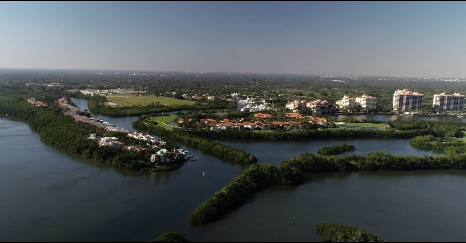 Aerial view of a waterfront Florida community with red-roofed buildings and mangroves.
