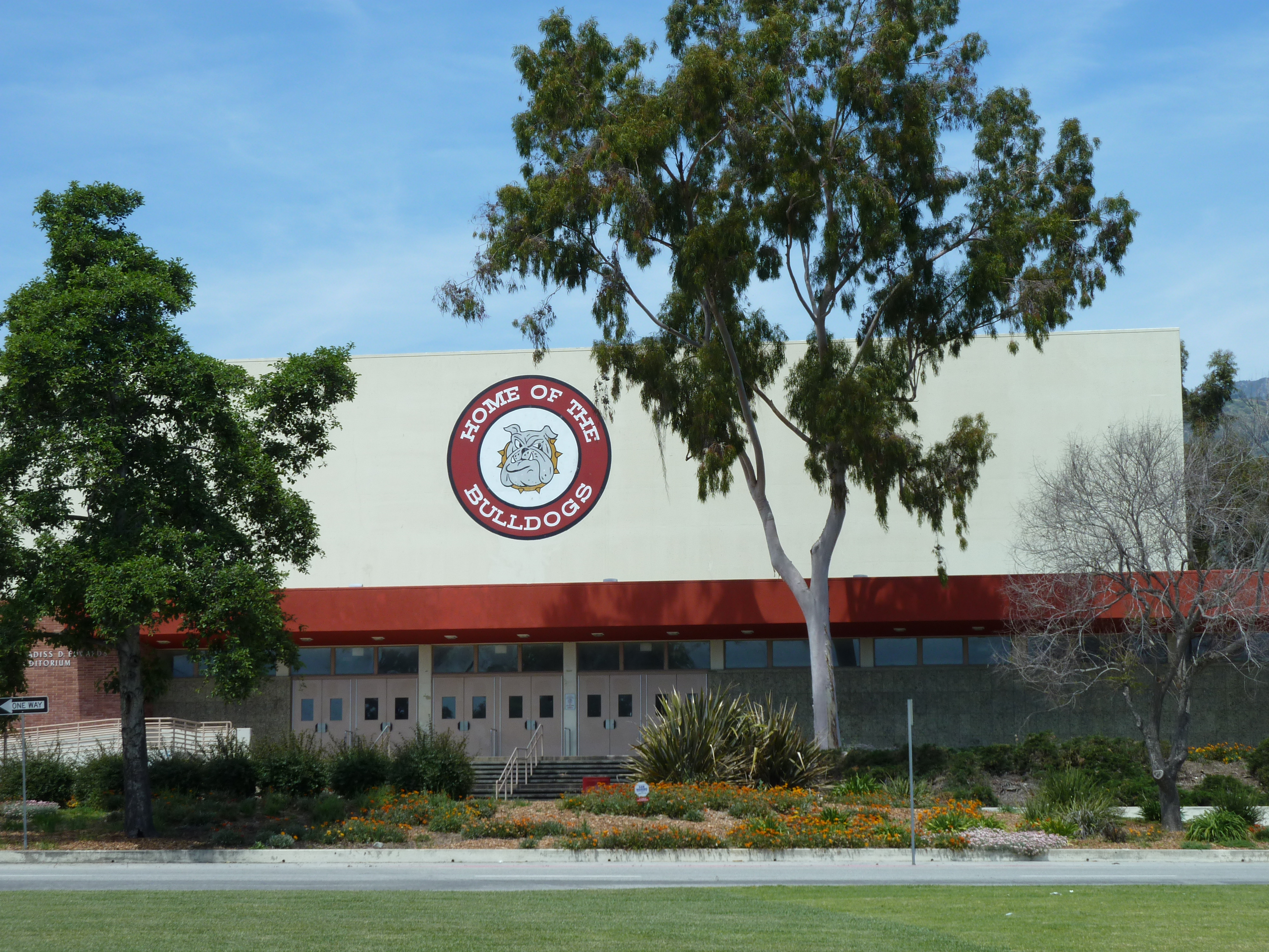 School building facade with a circular Bulldogs sign, trees, and partly cloudy sky.