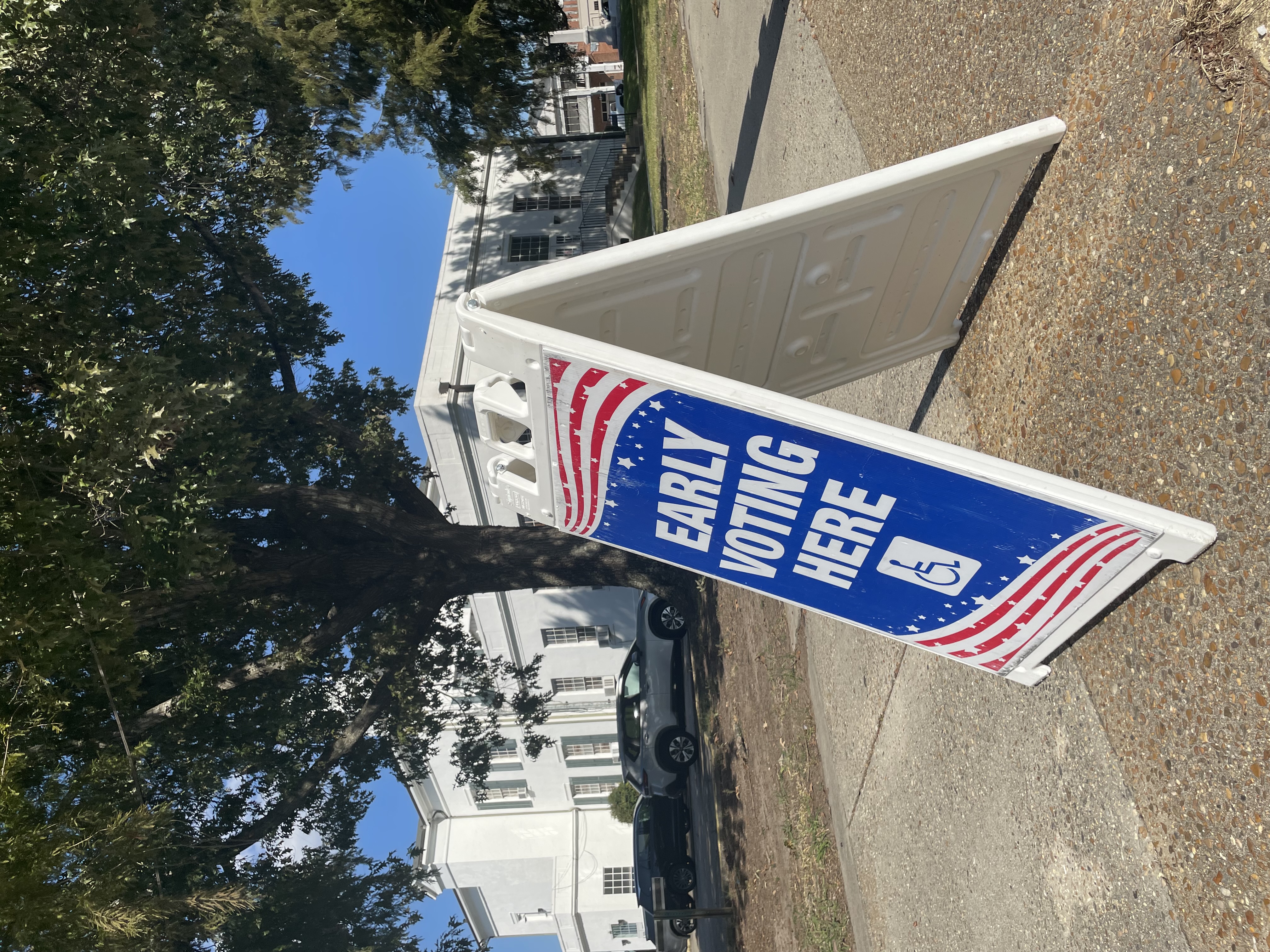 A-frame sign reading 'Early Voting Here' with an accessibility symbol on a sidewalk.