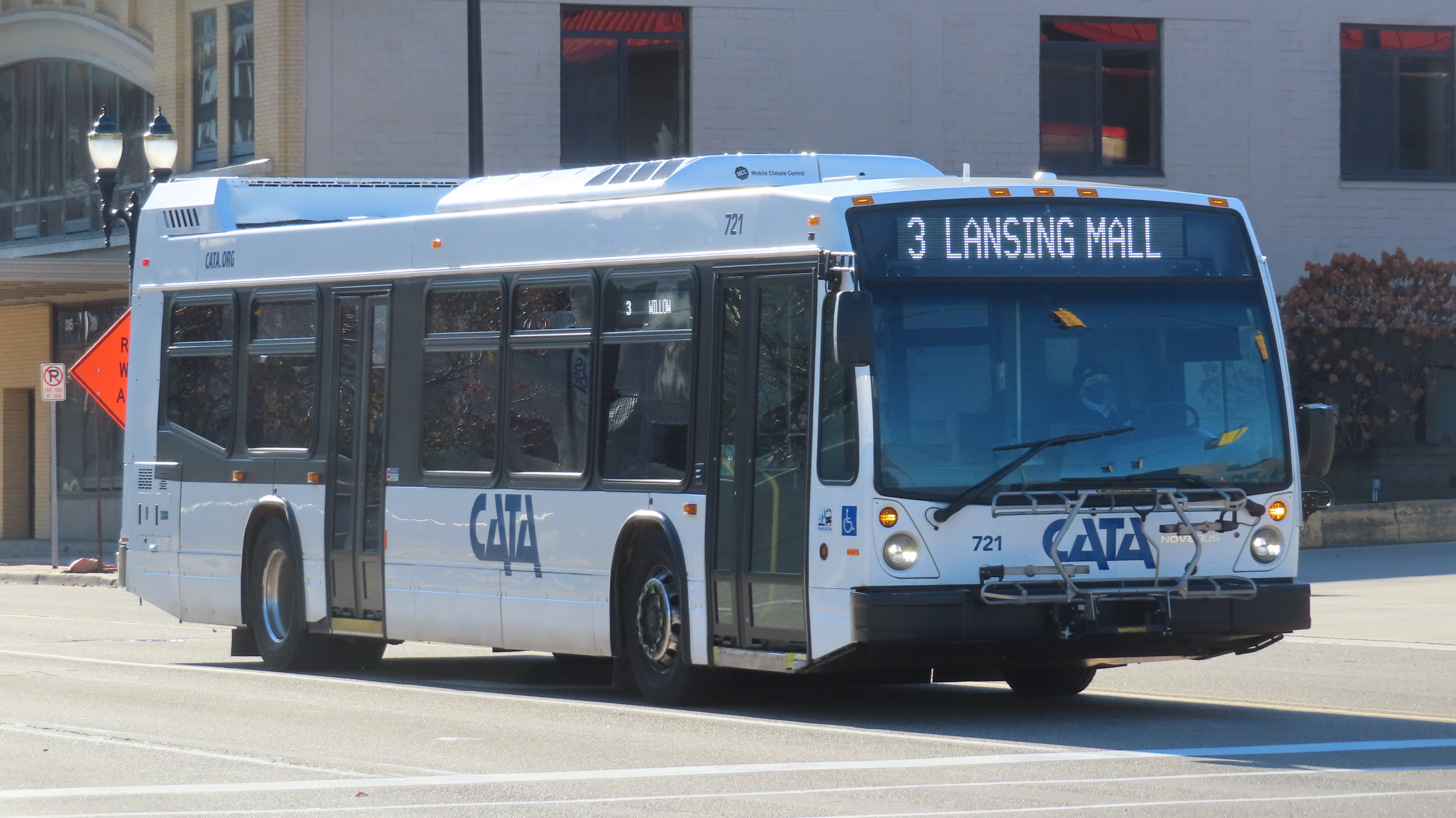 A white CATA transit bus travels along a downtown city street.