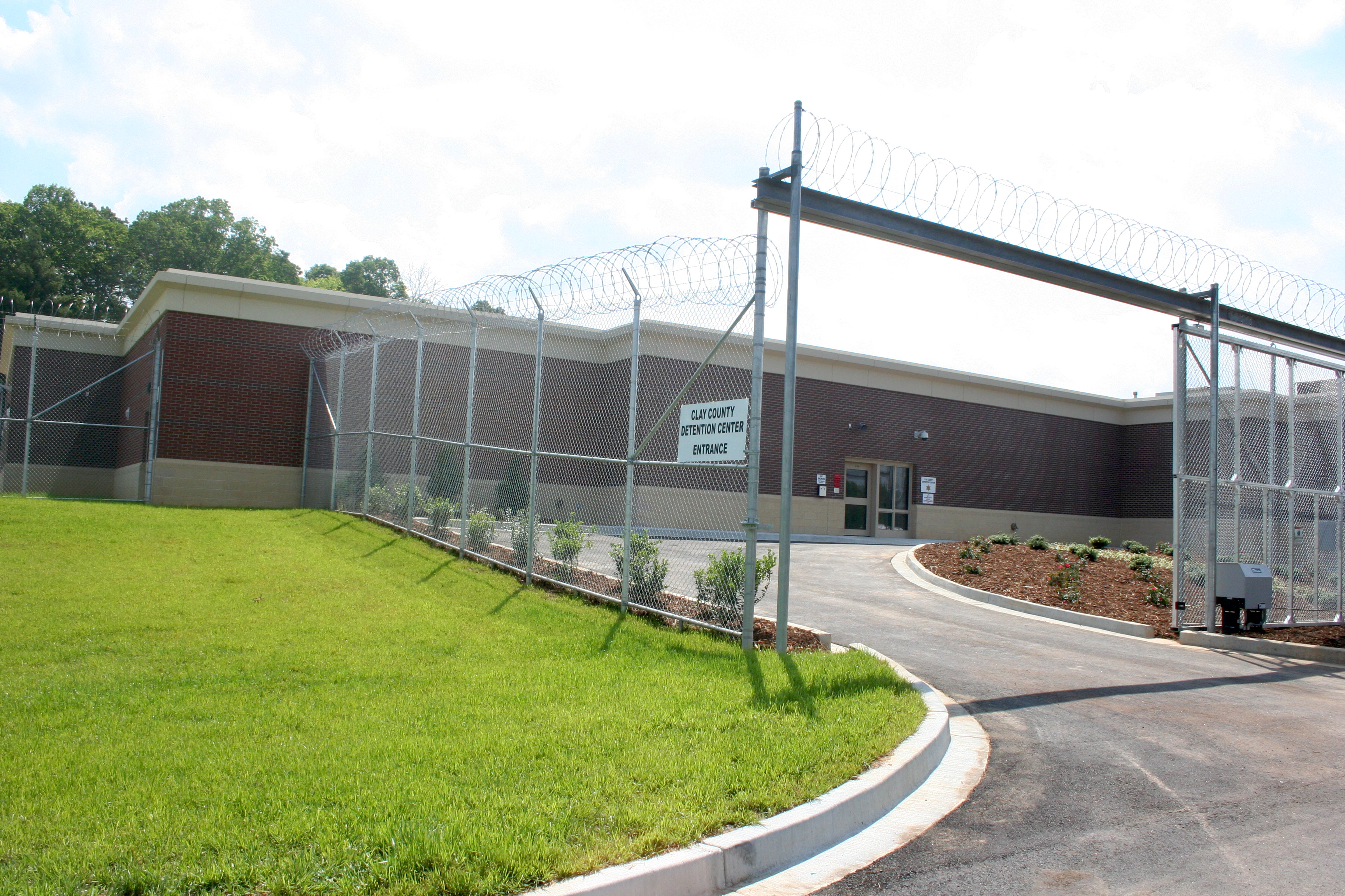 Low-profile detention center building enclosed by chain-link fence with razor wire on top.