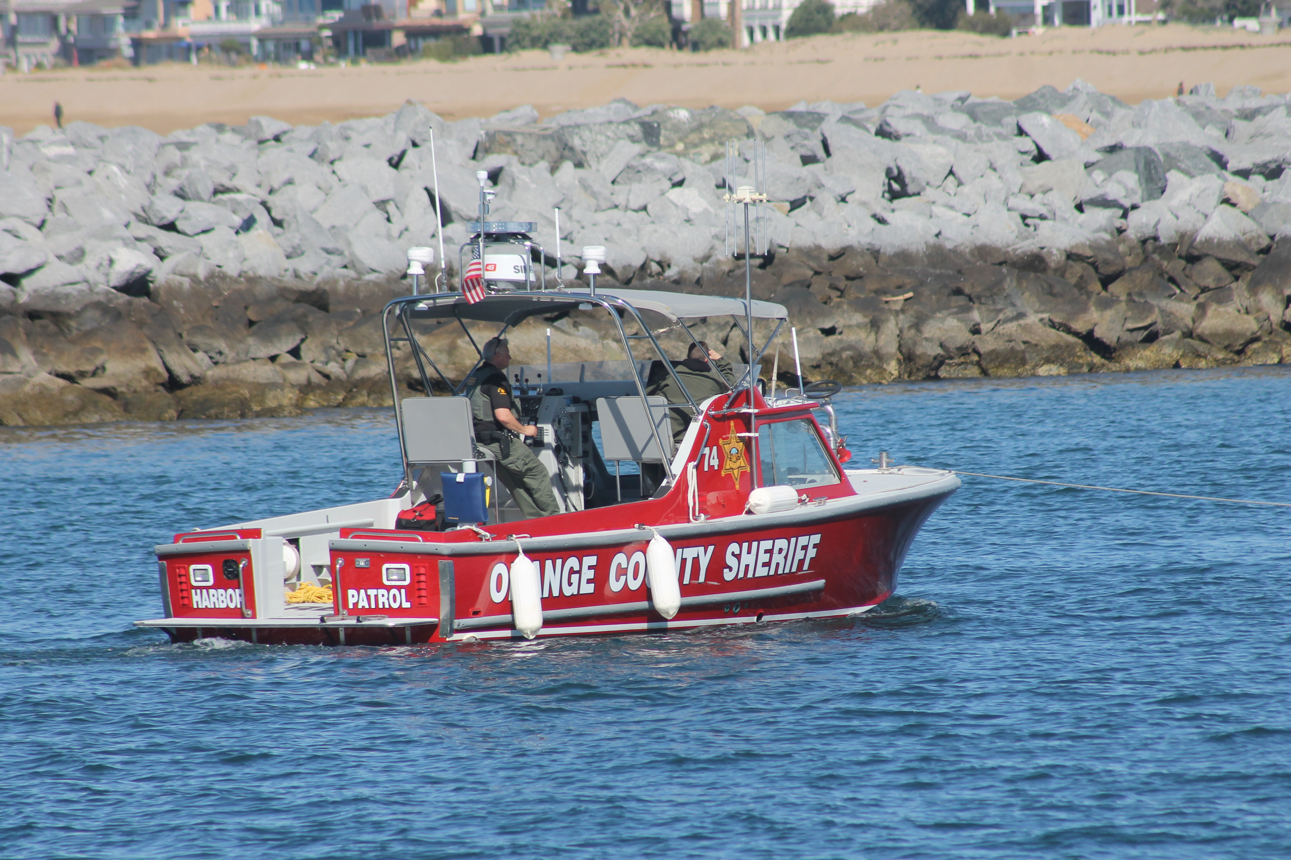 Red sheriff's harbor patrol boat numbered 74 near a rocky breakwater.