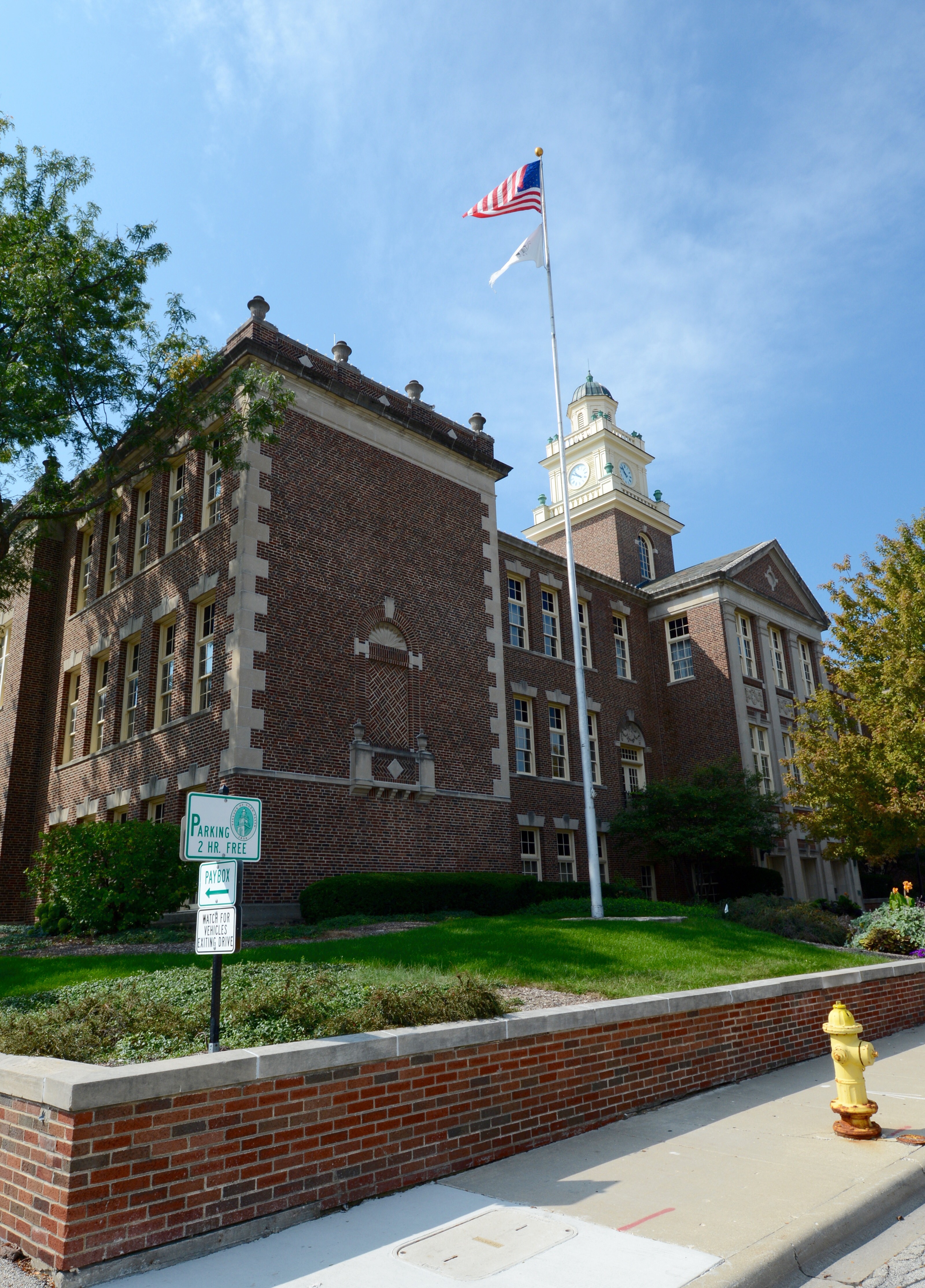 Large brick school building with clock tower and American flag on a sunny day.